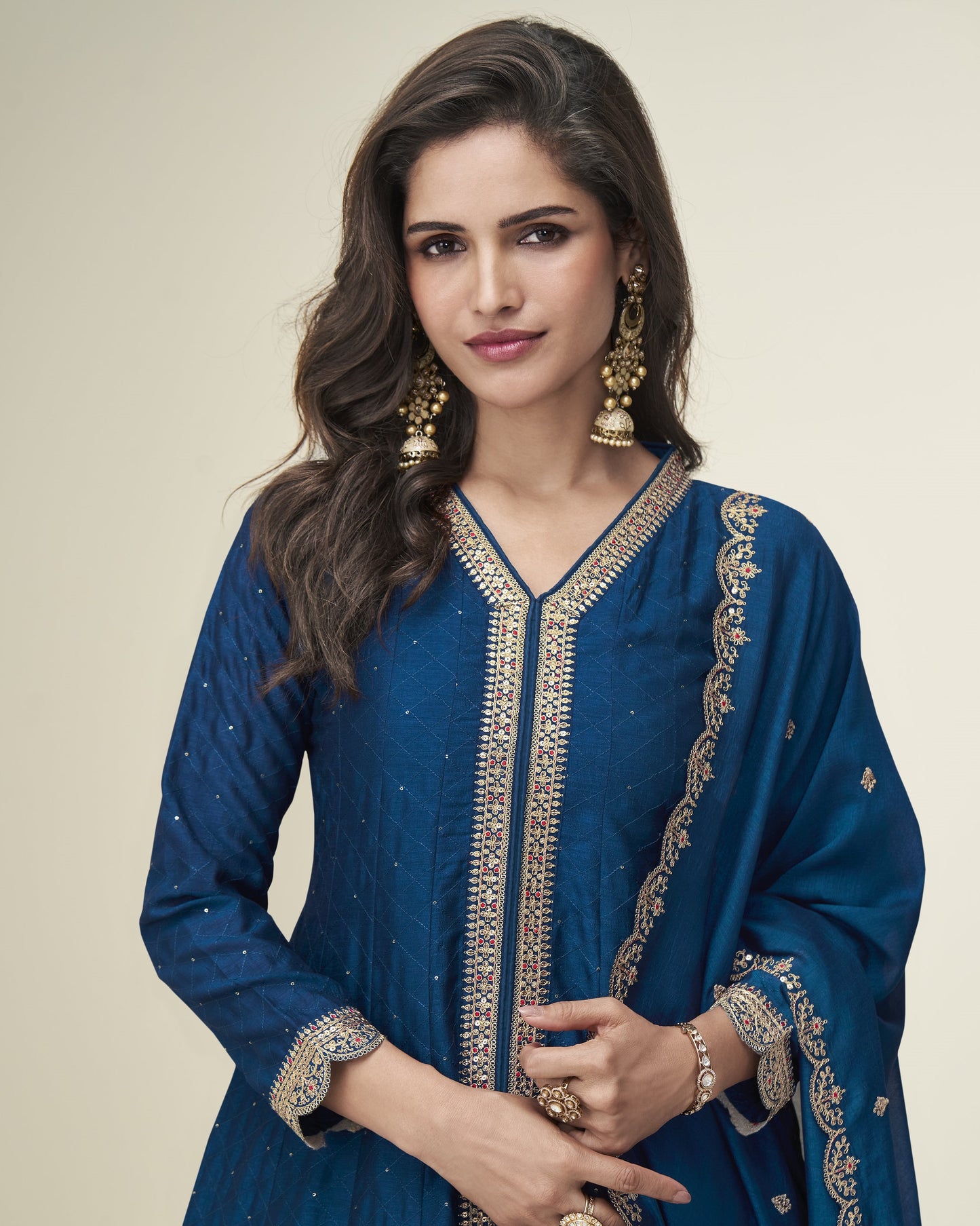 Woman wearing a blue embroidered dress with gold details on a beige background