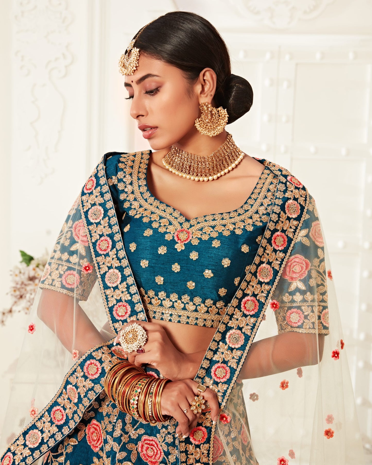 Woman in traditional blue and gold saree with jewelry against a white background