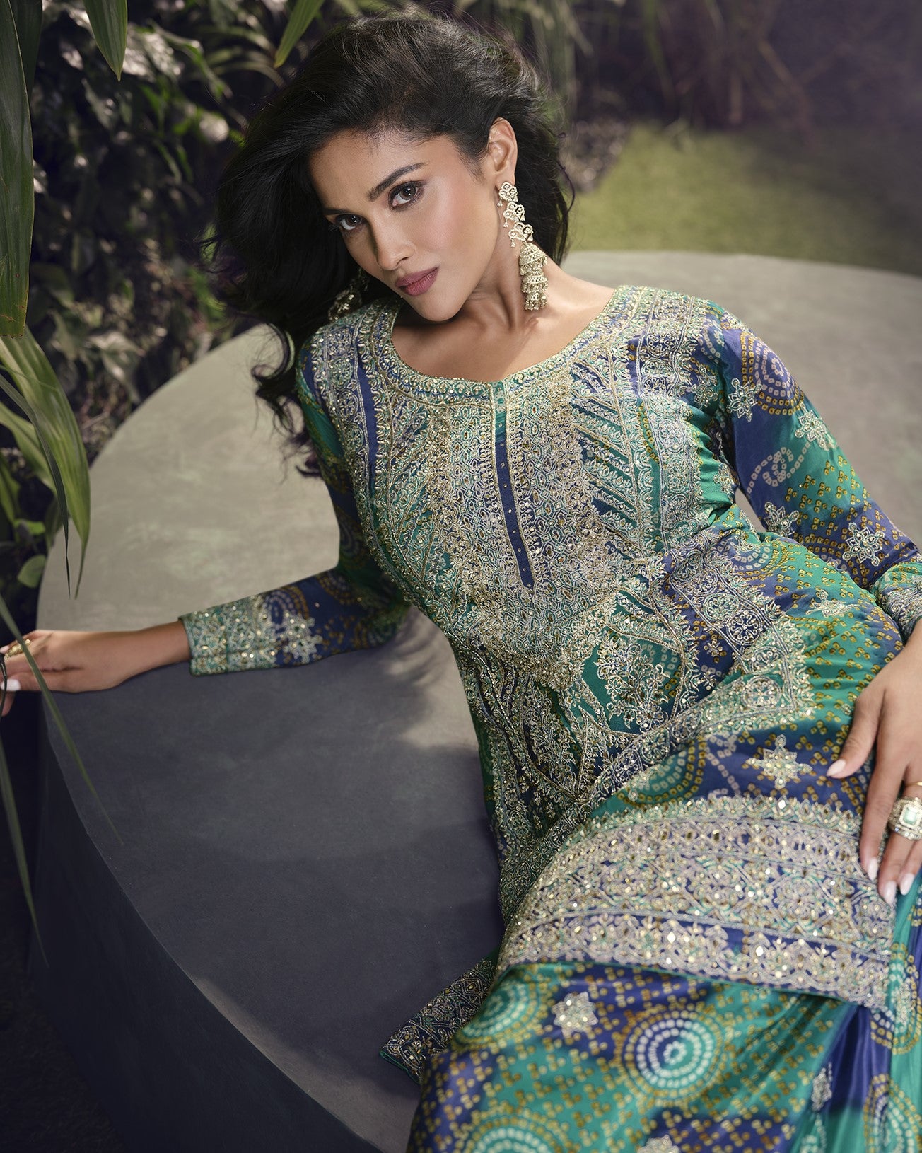 Woman wearing a patterned dress with jewelry, sitting outdoors.
