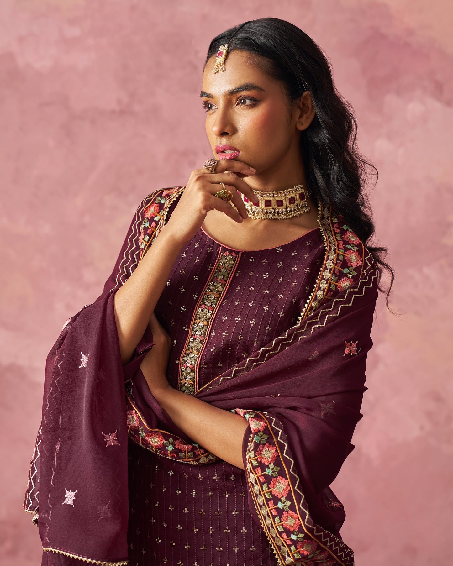 Woman wearing a traditional maroon saree with floral patterns against a pink background