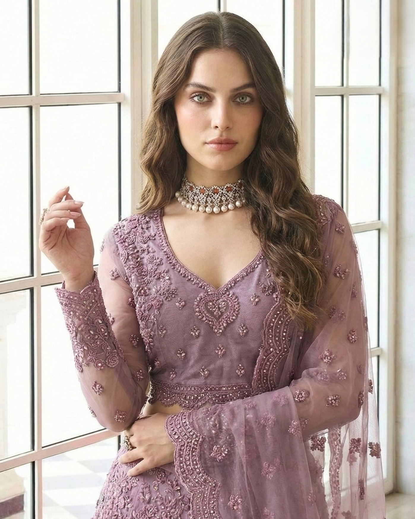 Woman wearing a purple embroidered dress with a necklace in front of a window.