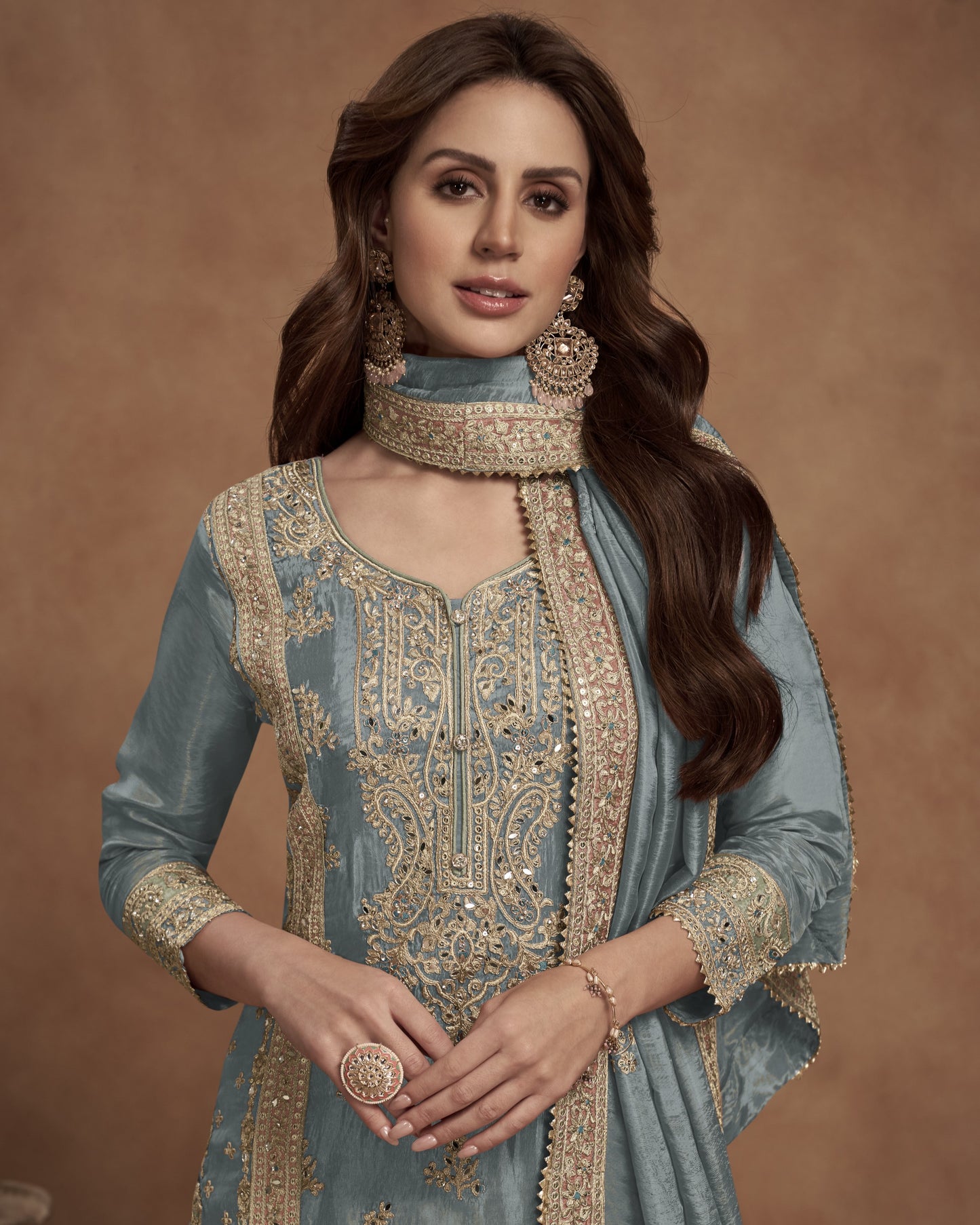 Woman wearing a traditional embroidered outfit with gold detailing against a brown background