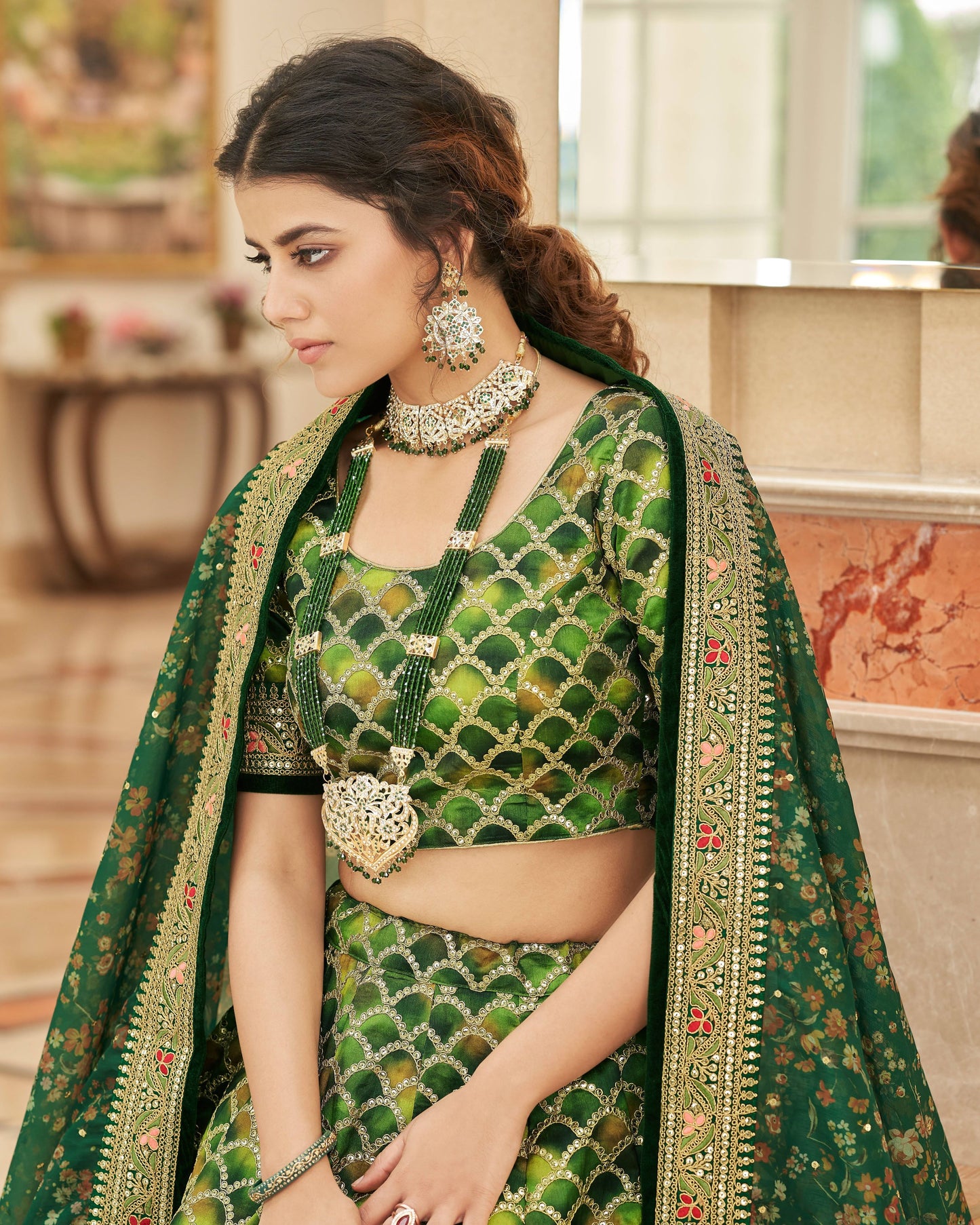 Woman wearing a green embroidered traditional outfit with jewelry indoors.