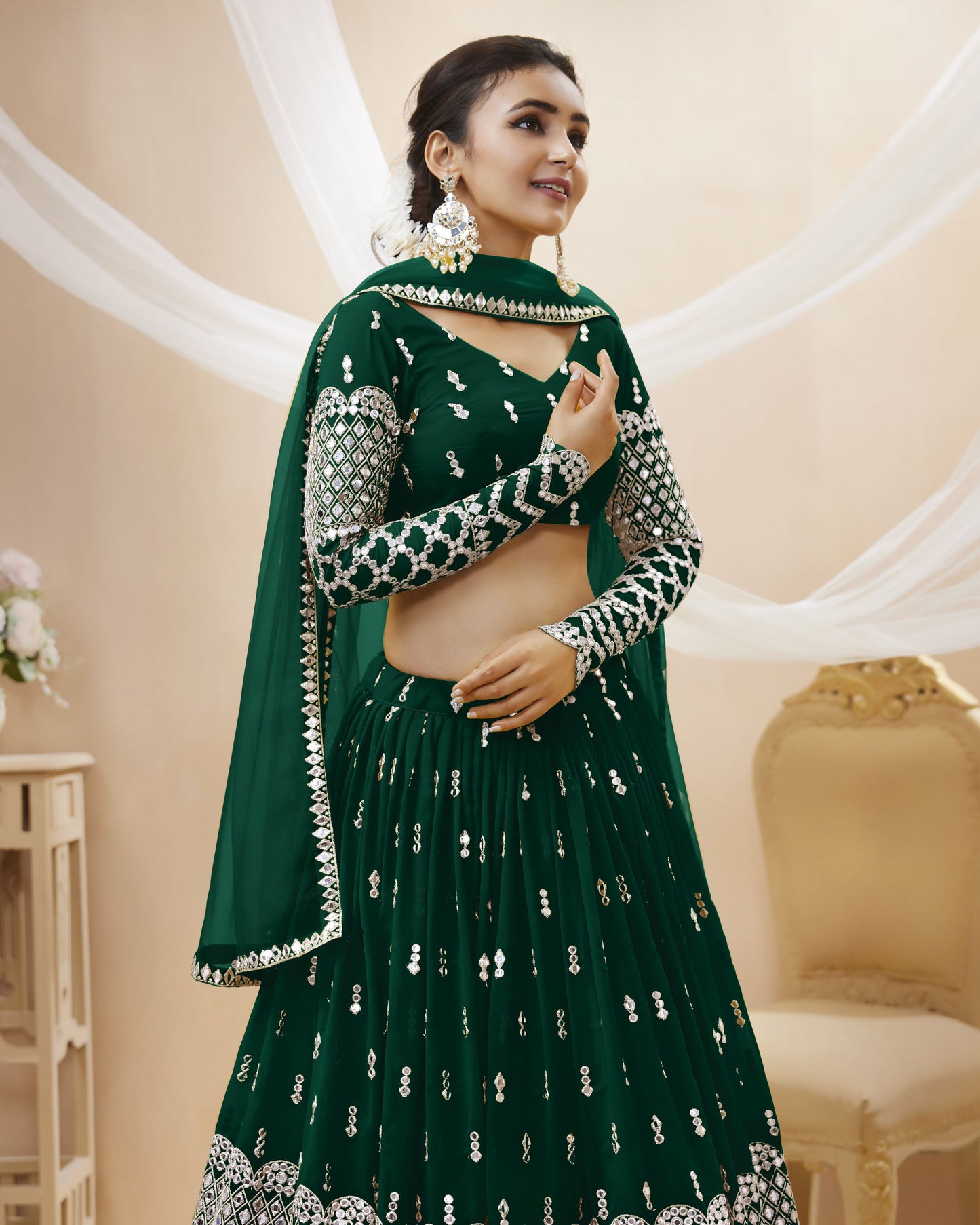 Woman wearing a green traditional outfit with silver embroidery in an elegant indoor setting.
