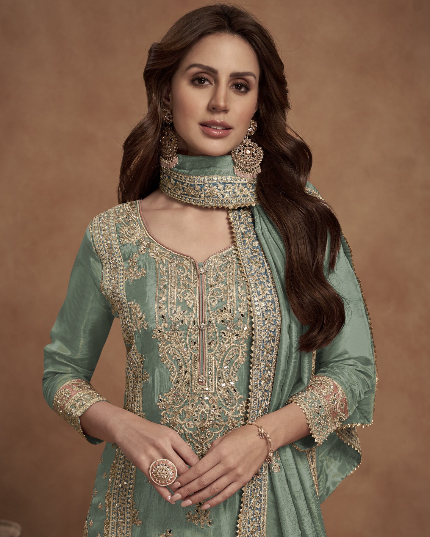 Woman wearing a traditional green embroidered outfit with jewelry against a brown background