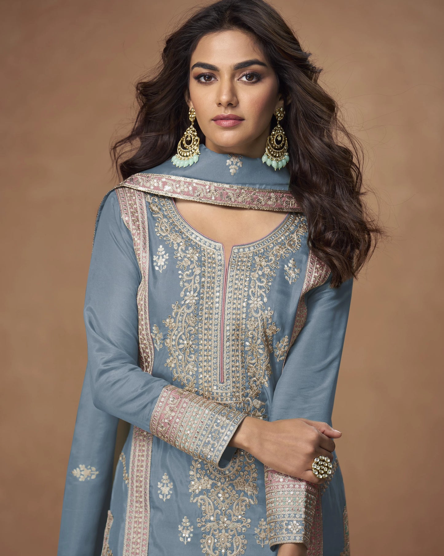 Woman wearing a blue embroidered traditional outfit with jewelry against a brown background