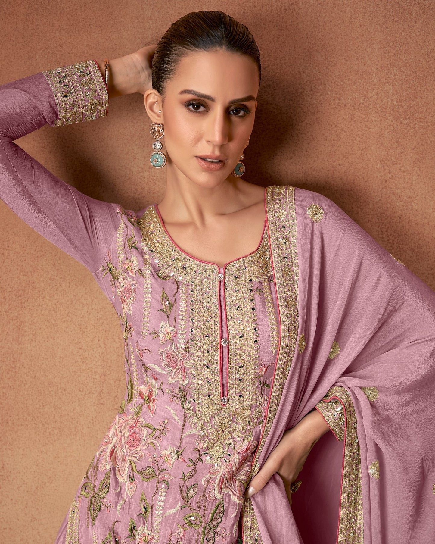Woman wearing a pink embroidered traditional outfit against a brown background