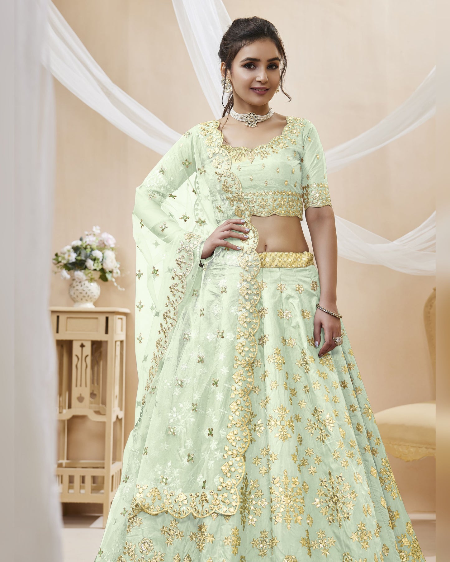 Woman wearing a light green embroidered traditional outfit with gold details in a decorated room.