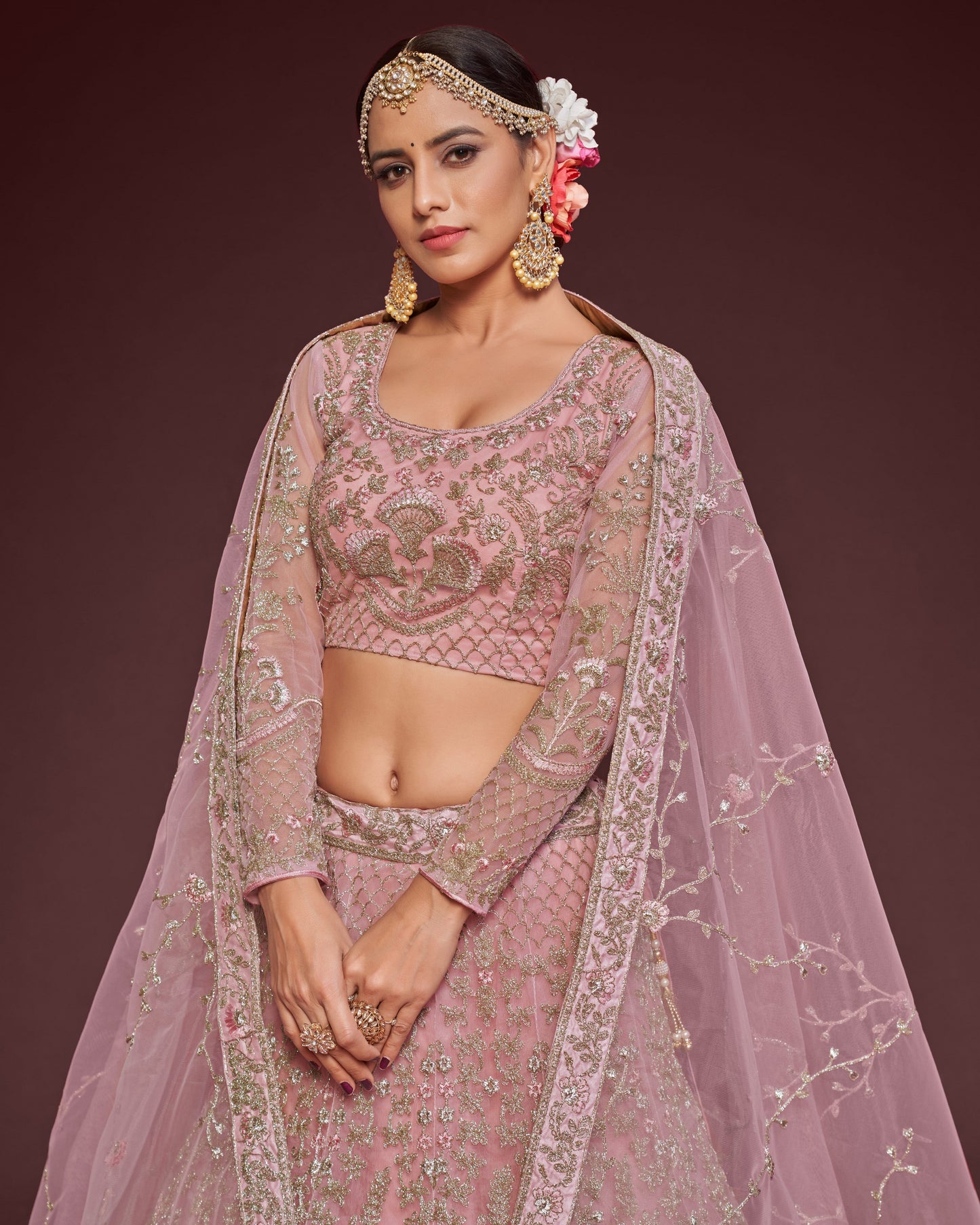 Woman in traditional pink embroidered outfit with a floral headpiece against a dark background
