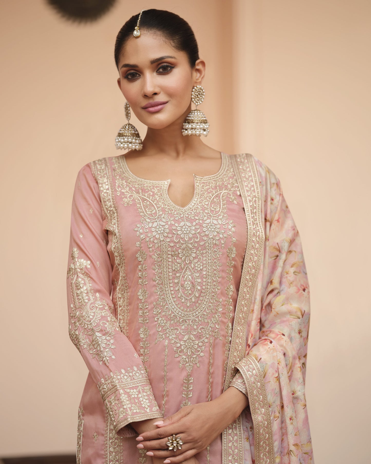 Woman wearing a traditional pink and gold embroidered outfit with a plain background