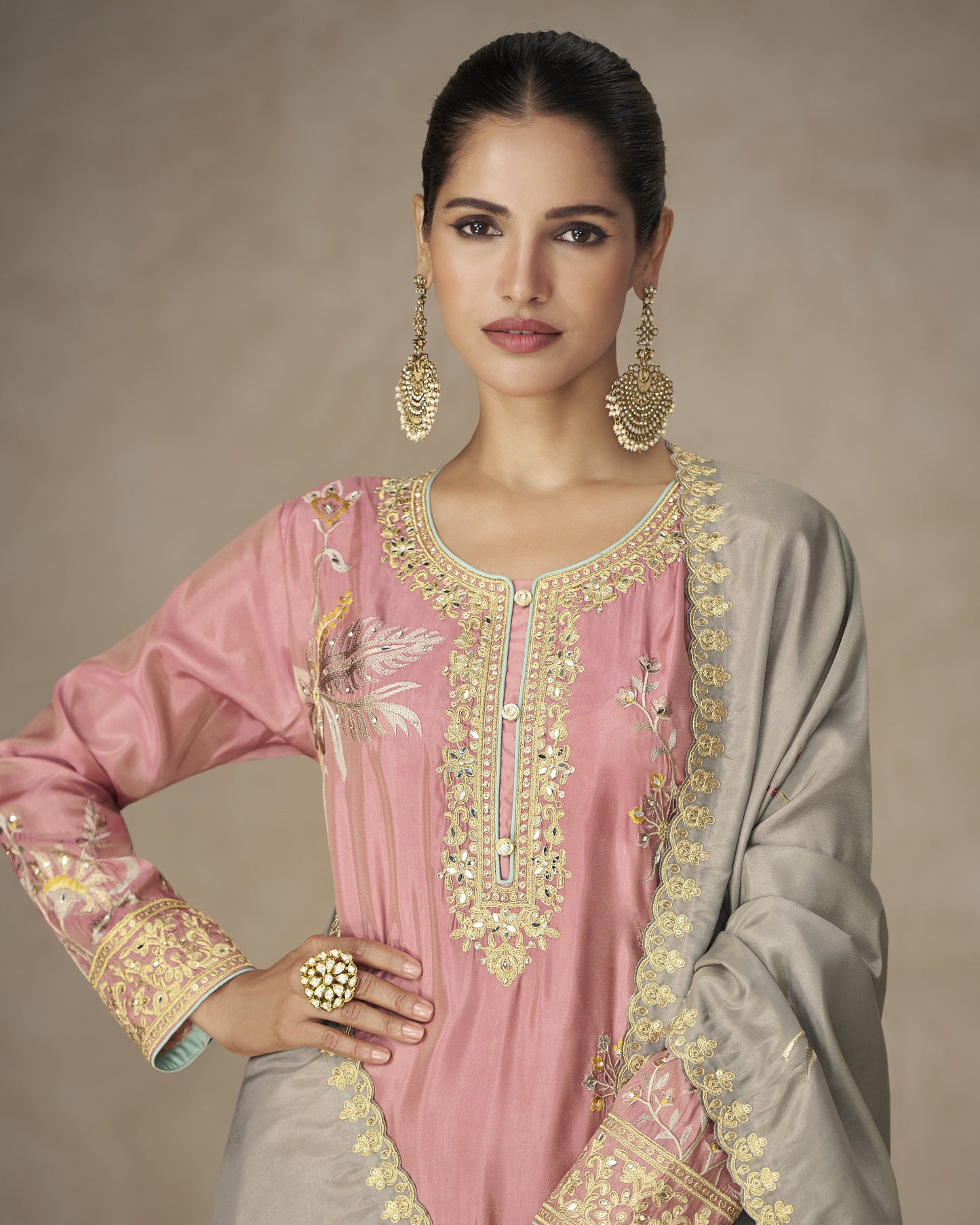 Woman wearing a pink and gray embroidered traditional outfit with gold detailing on a beige background