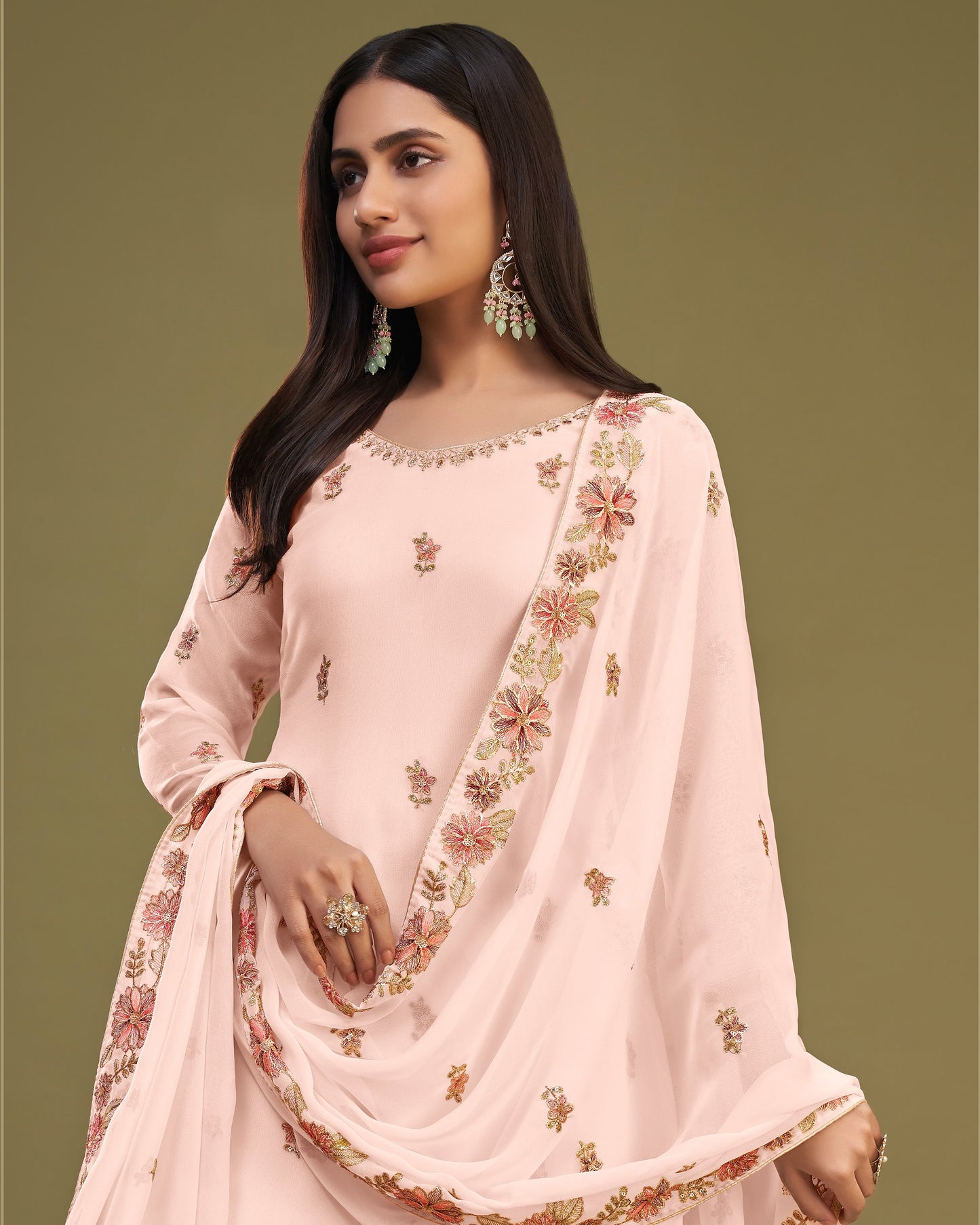 Woman wearing a light pink traditional outfit with floral embroidery on a green background