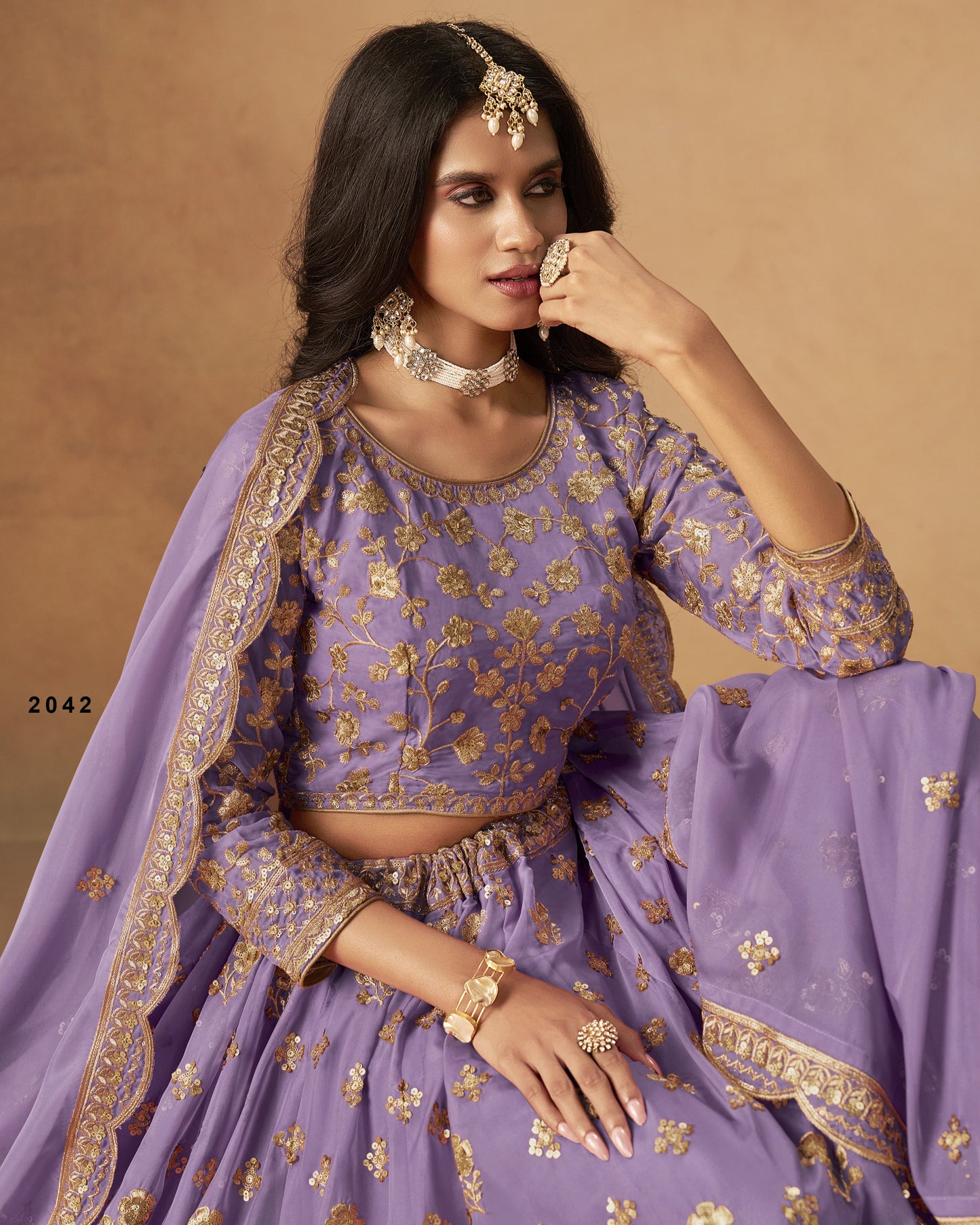 Woman in a purple traditional outfit with gold embroidery against a beige background