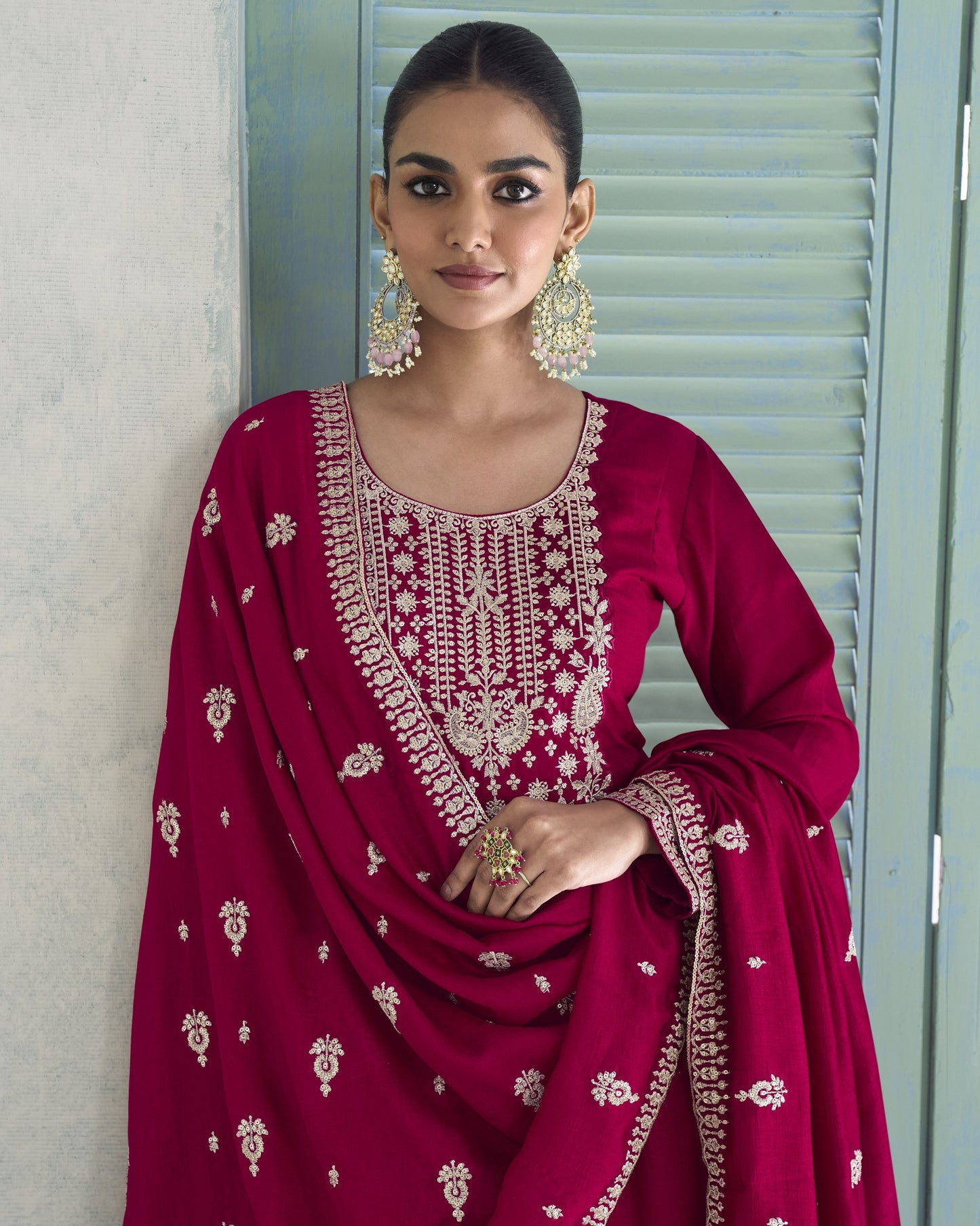 Woman wearing a red embroidered traditional outfit with gold jewelry indoors.