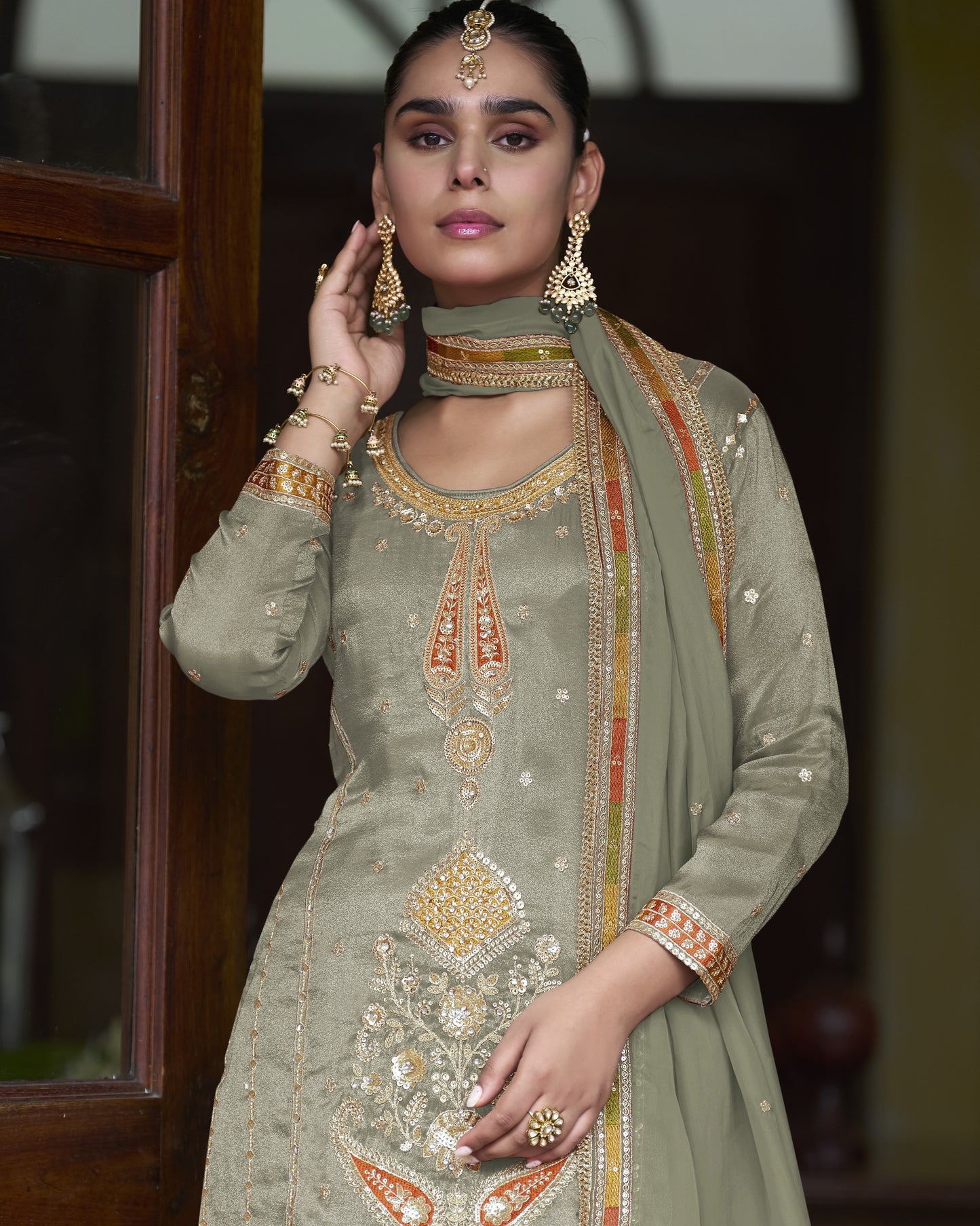 Woman wearing a traditional olive green outfit with gold embroidery indoors.