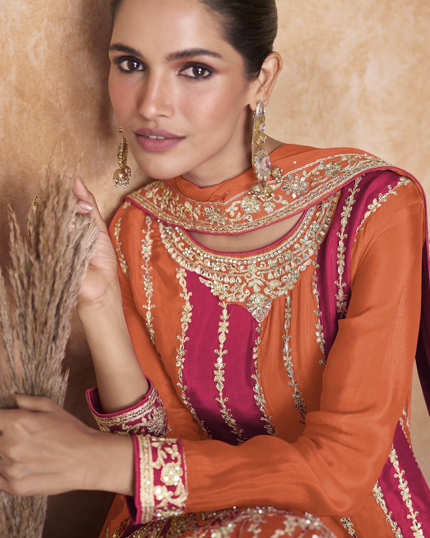 Woman wearing an orange and pink embroidered traditional outfit with a beige background