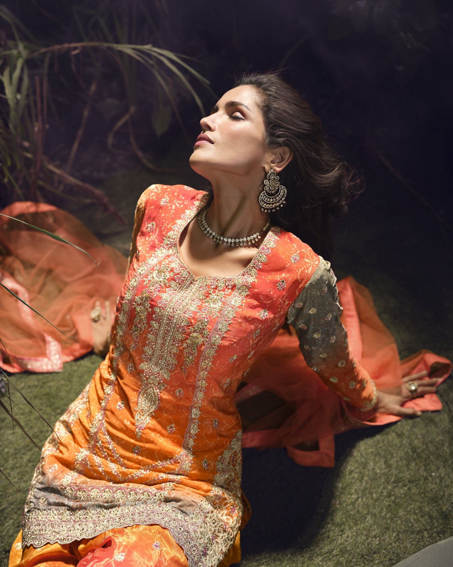 Woman in traditional orange and silver embroidered outfit sitting on grass