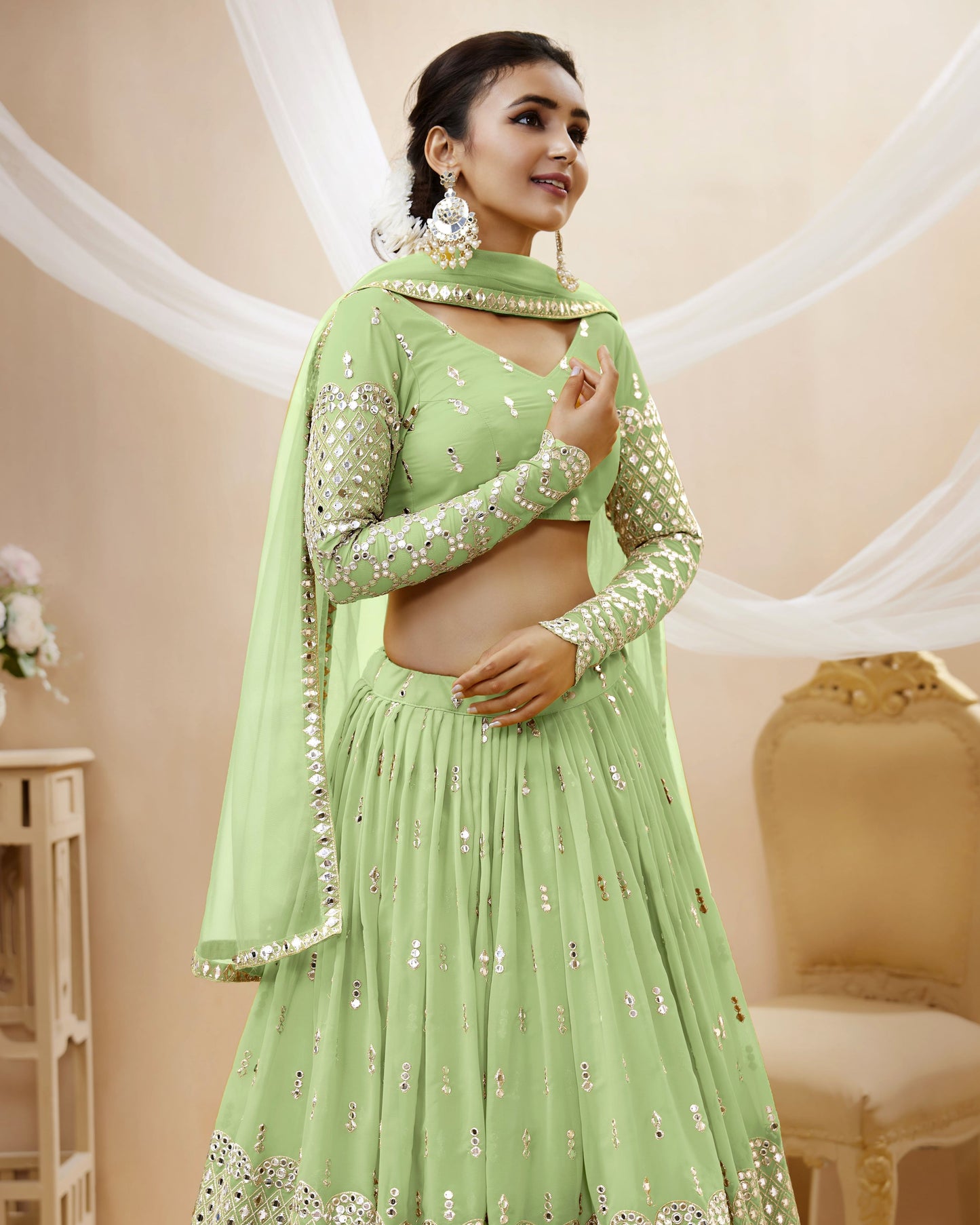 Woman wearing a light green traditional outfit with a matching dupatta in a decorated room.