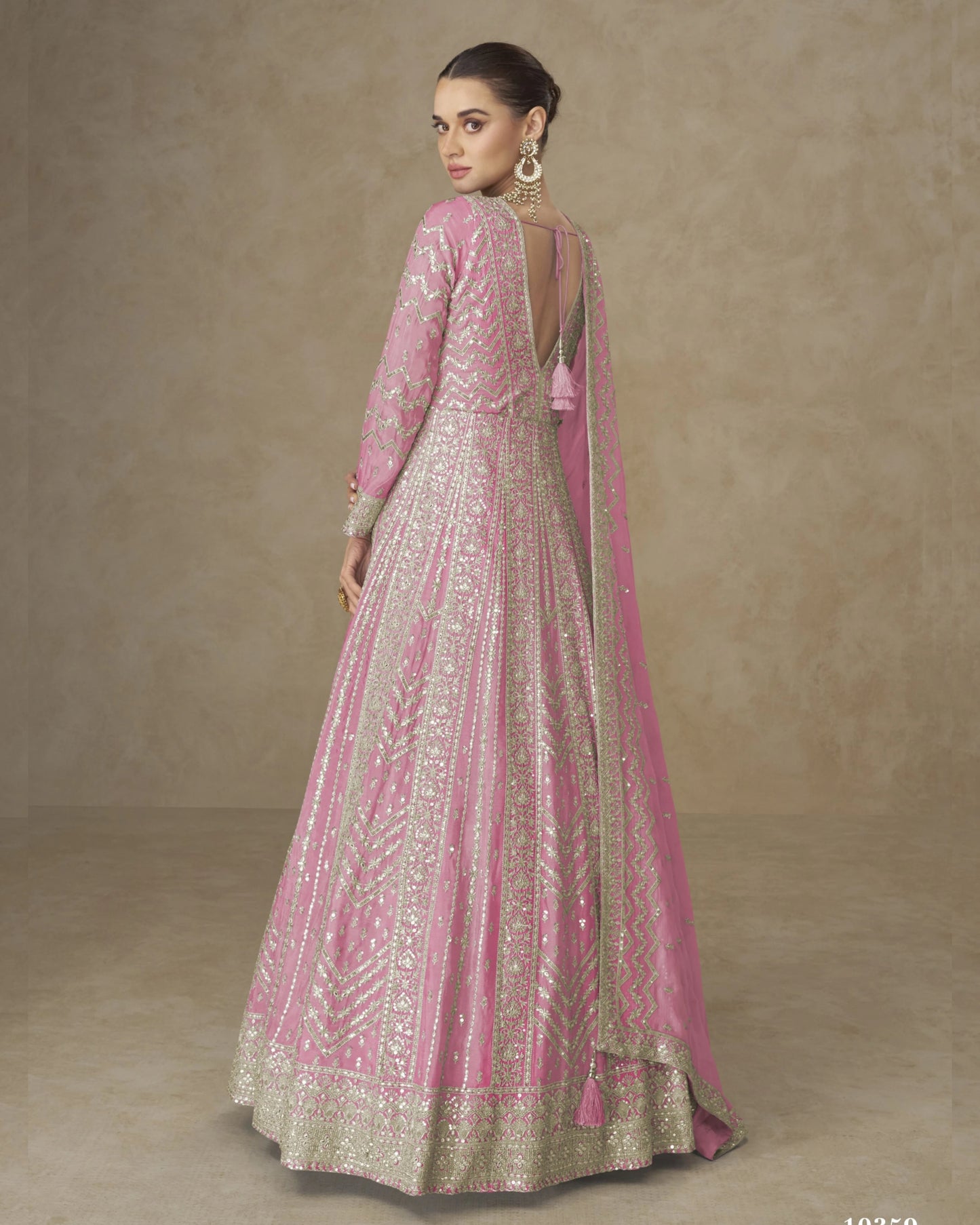 Woman wearing a pink and gold traditional outfit against a beige background