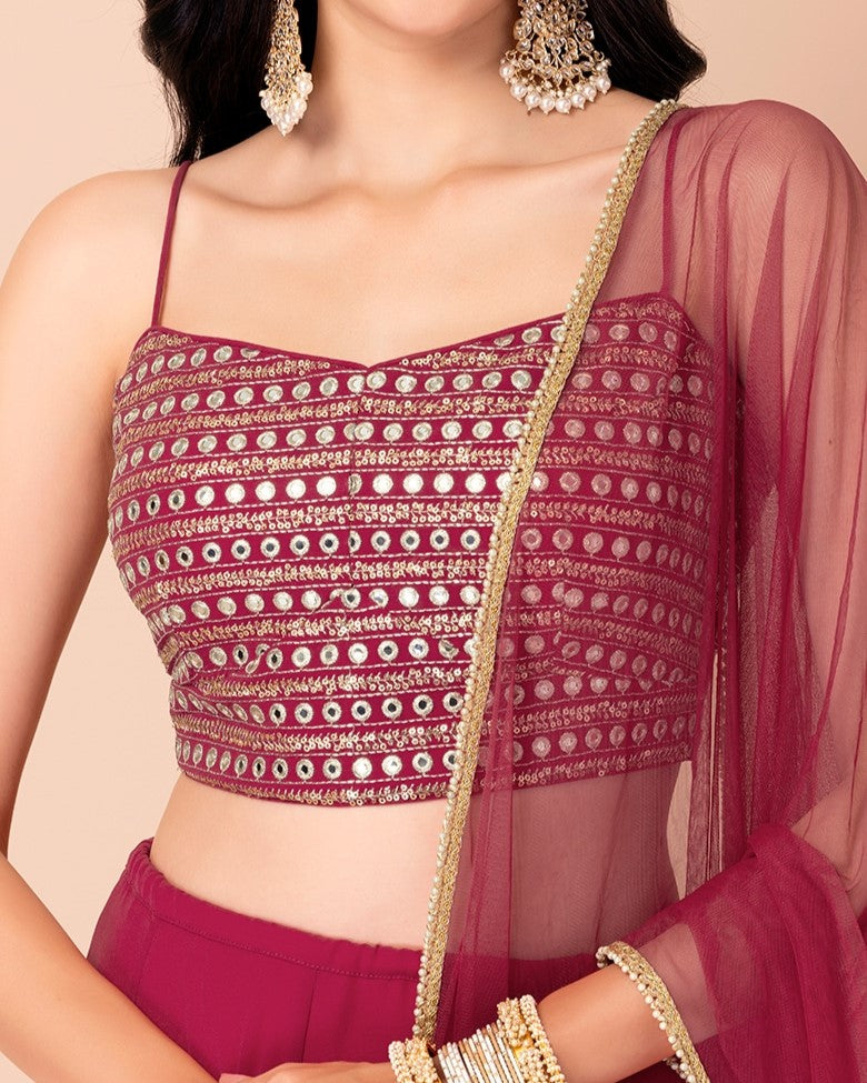 Woman wearing a maroon patterned top with gold accents and a sheer dupatta on a beige background