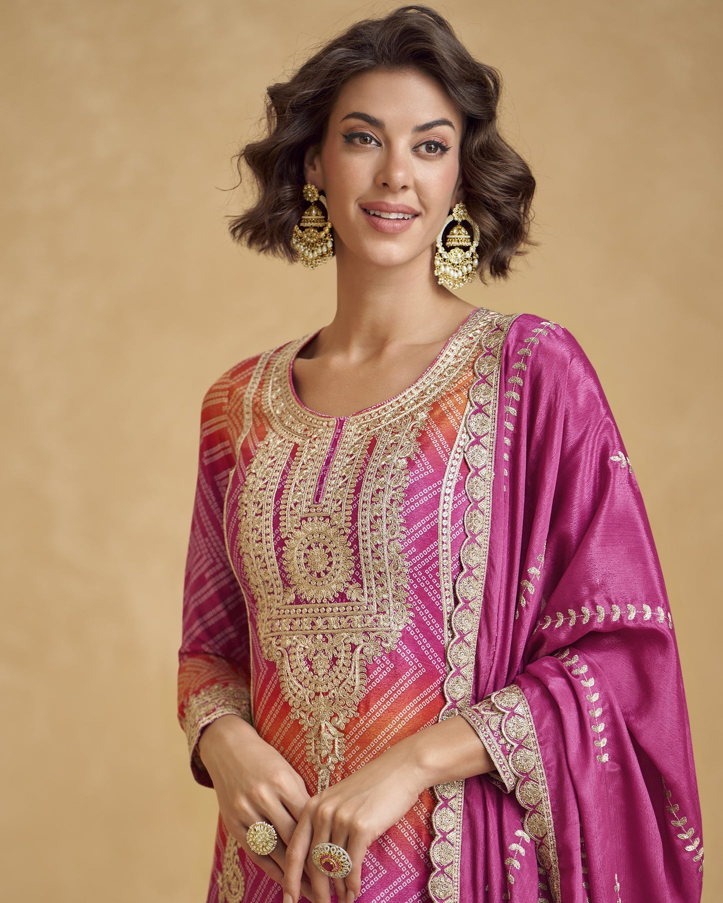 Woman wearing a traditional embroidered outfit with a pink dupatta against a beige background