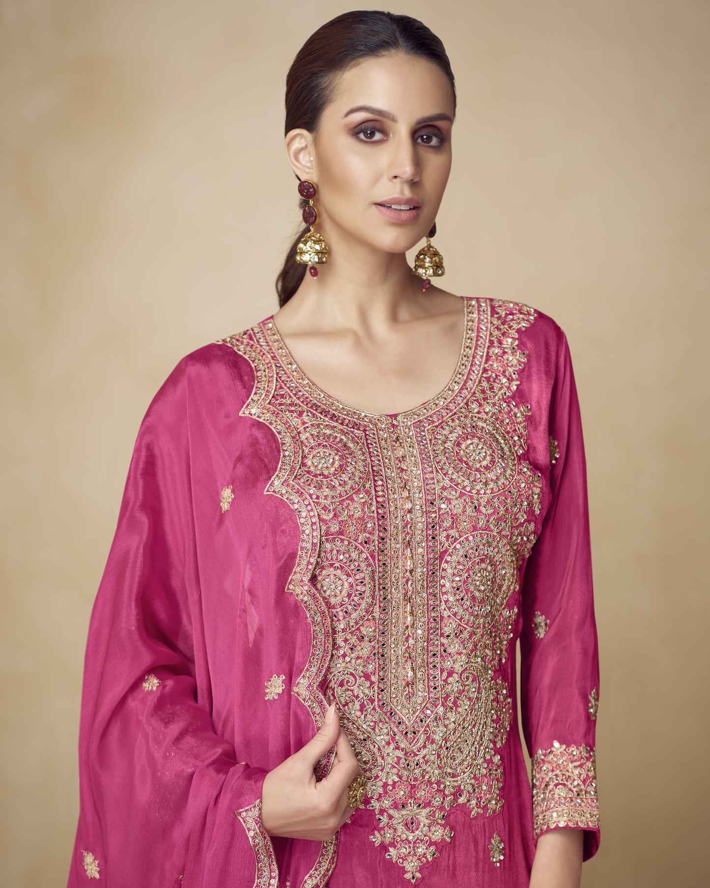 Woman wearing a pink embroidered traditional outfit against a beige background