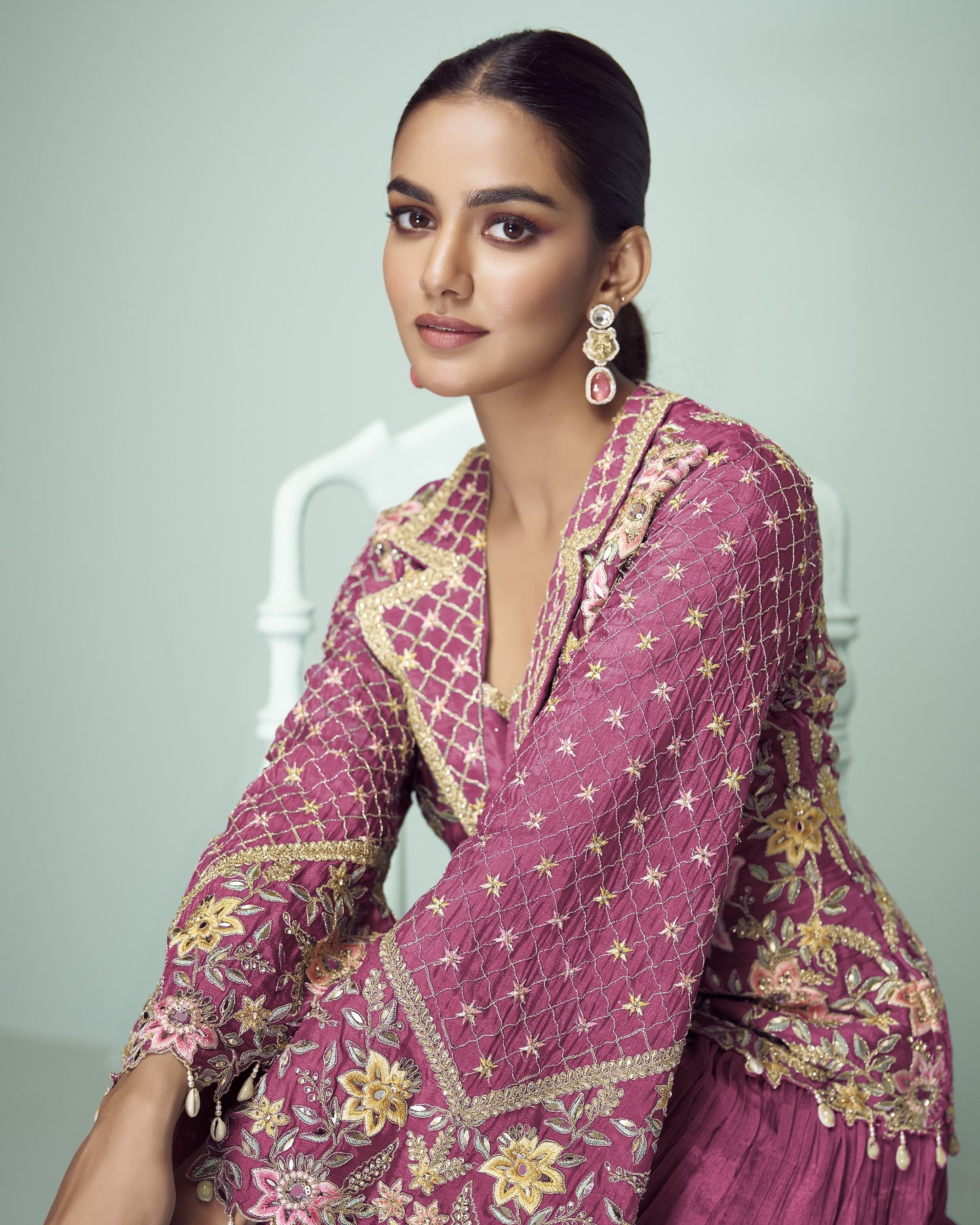 Woman wearing a pink embroidered traditional outfit with gold details on a light gray background
