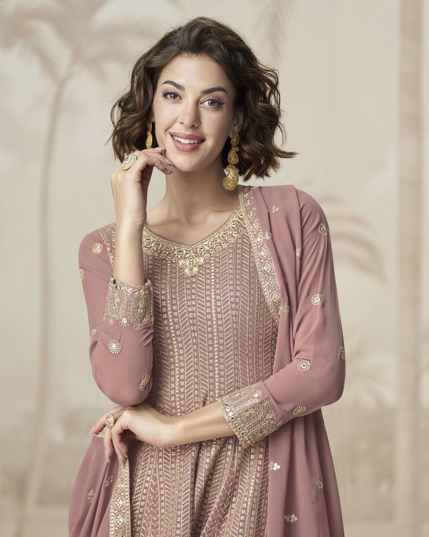 Woman wearing a pink embroidered outfit with gold details on a beige background