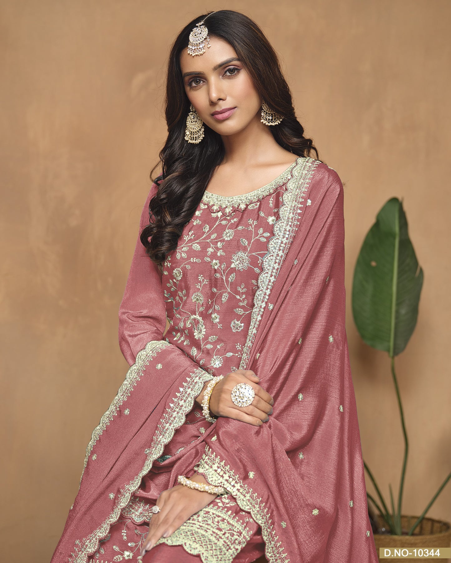 Woman wearing a traditional pink embroidered outfit with jewelry against a beige background