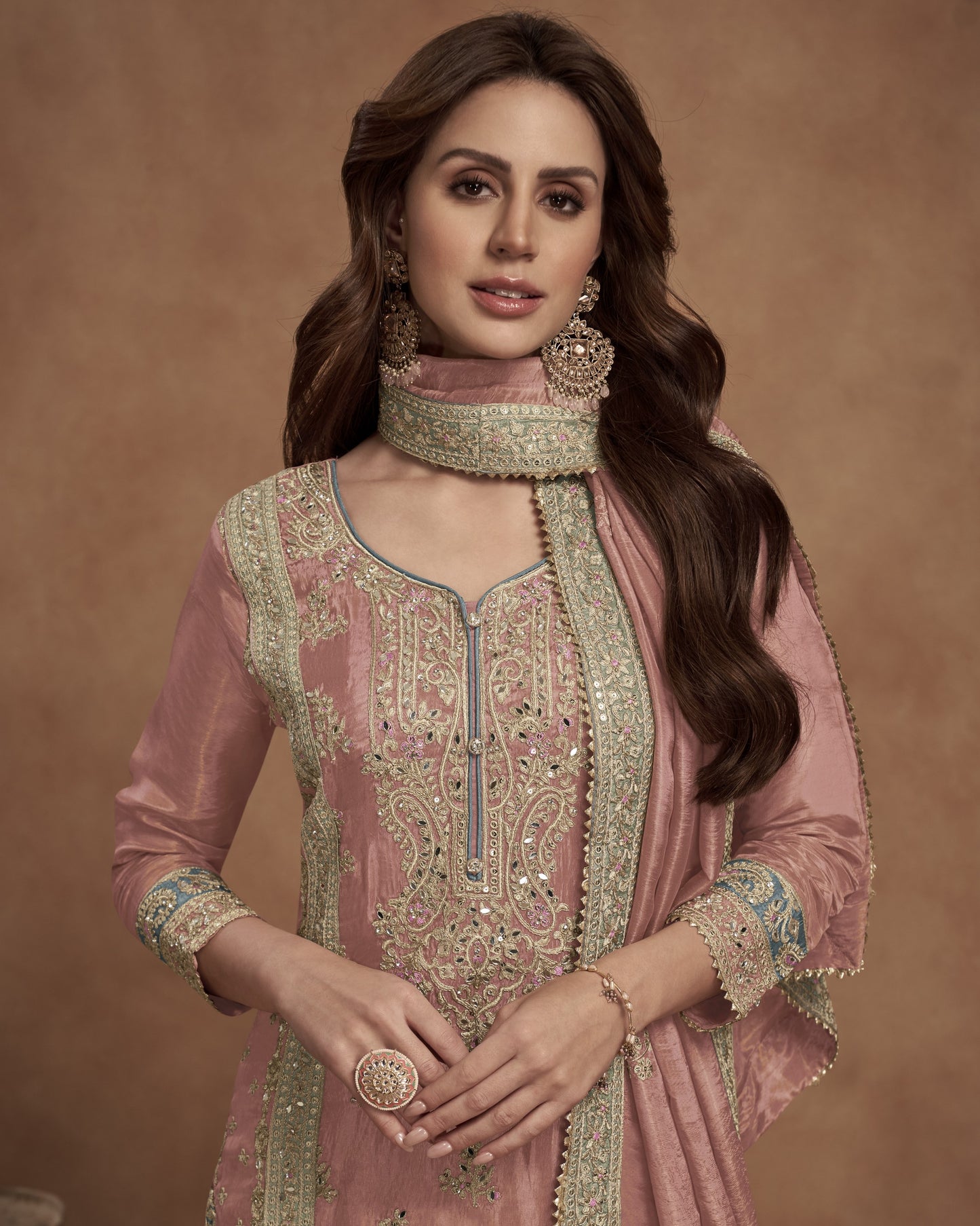 Woman wearing a pink embroidered traditional outfit with a brown background