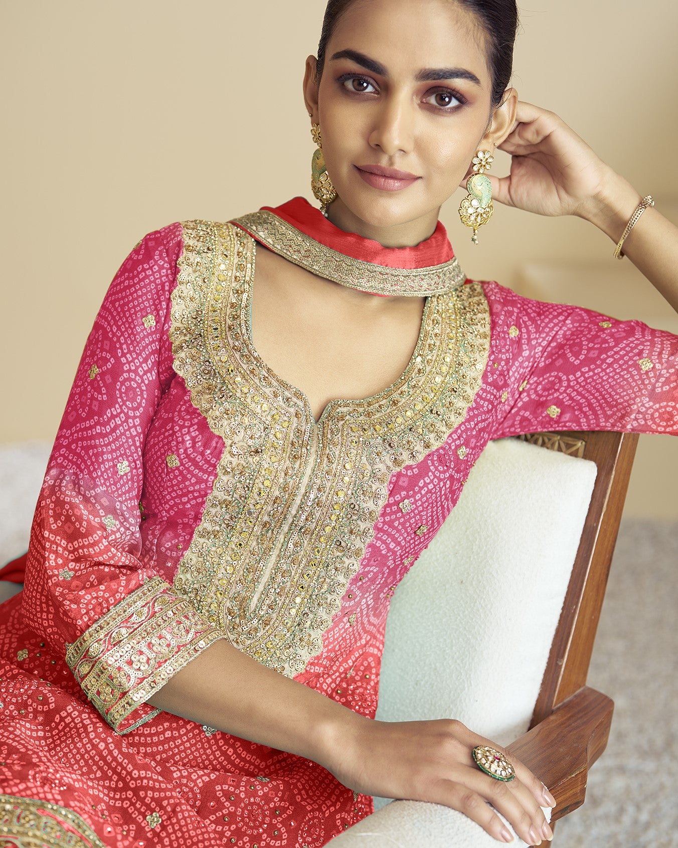 Woman wearing a pink and gold traditional outfit with jewelry, sitting on a white couch.