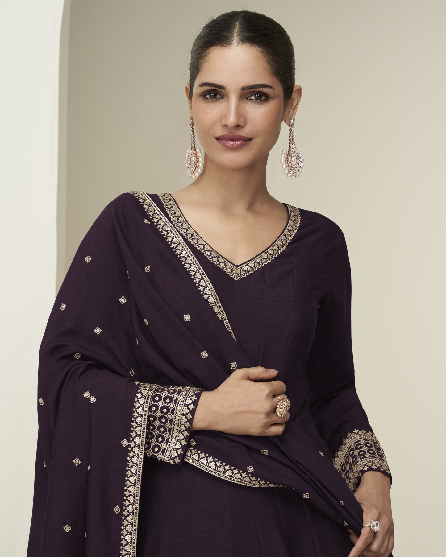 Woman wearing a dark purple traditional outfit with intricate embroidery on a neutral background