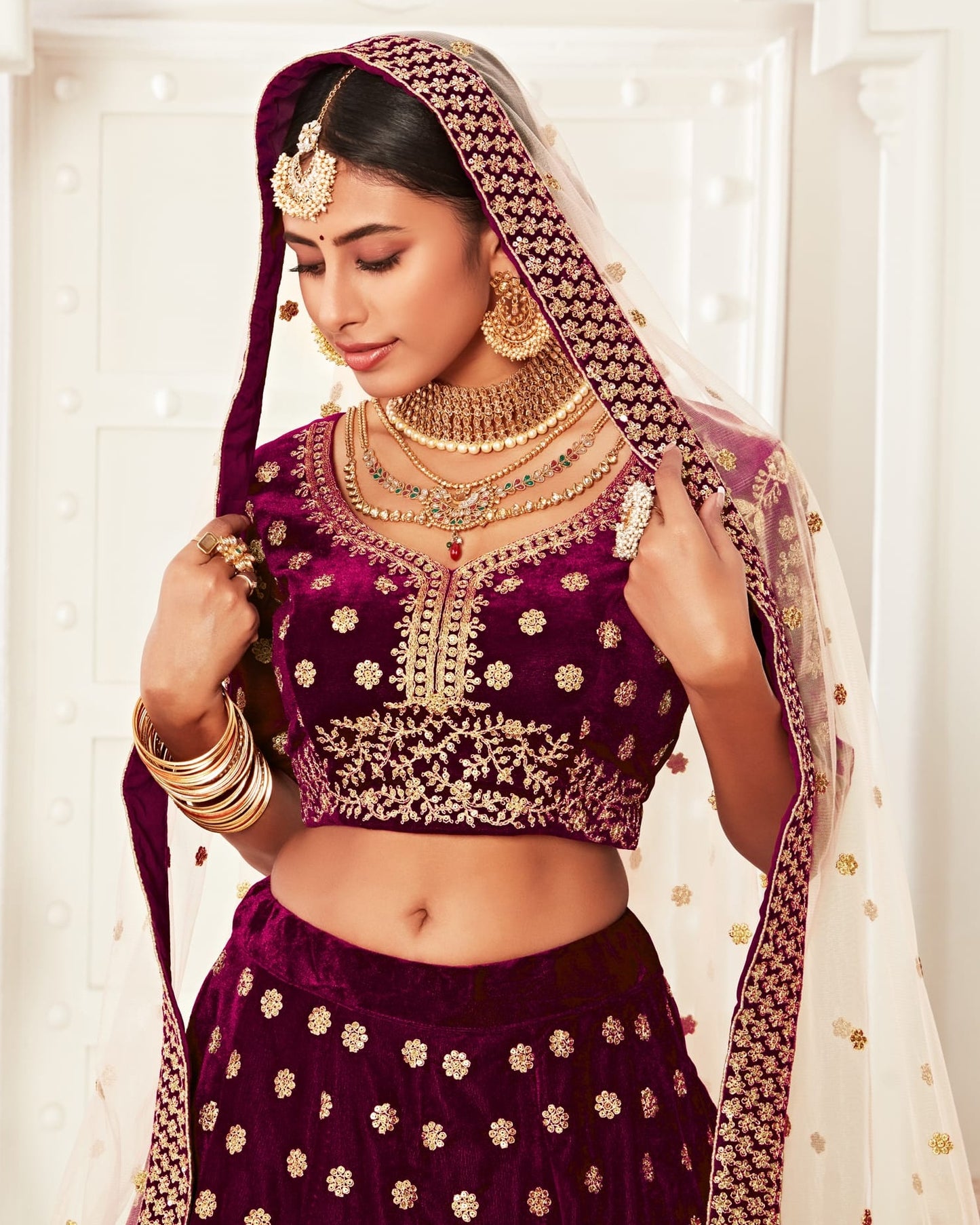 Woman in traditional purple and gold outfit with jewelry against a white background