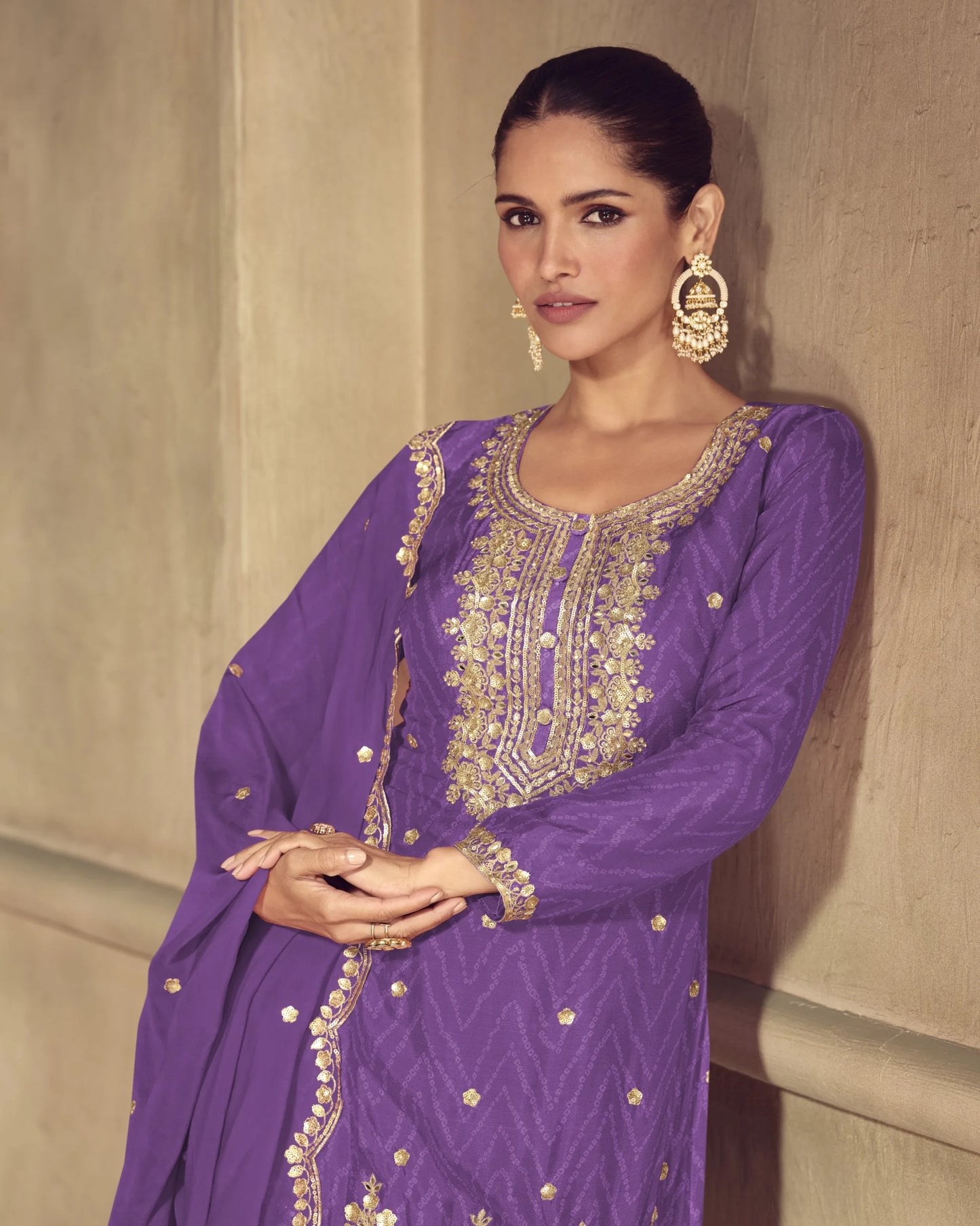 Woman wearing a purple embroidered traditional outfit against a beige wall.