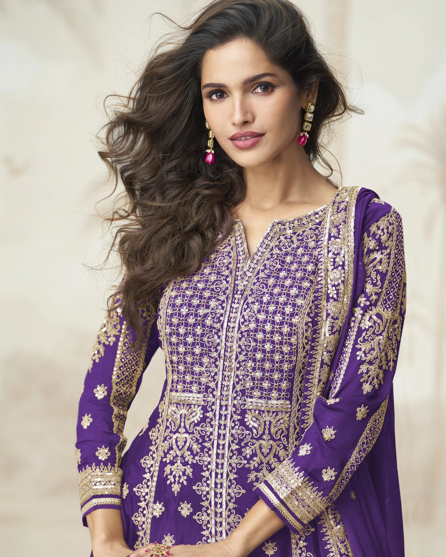Woman wearing a purple embroidered traditional outfit with a neutral background