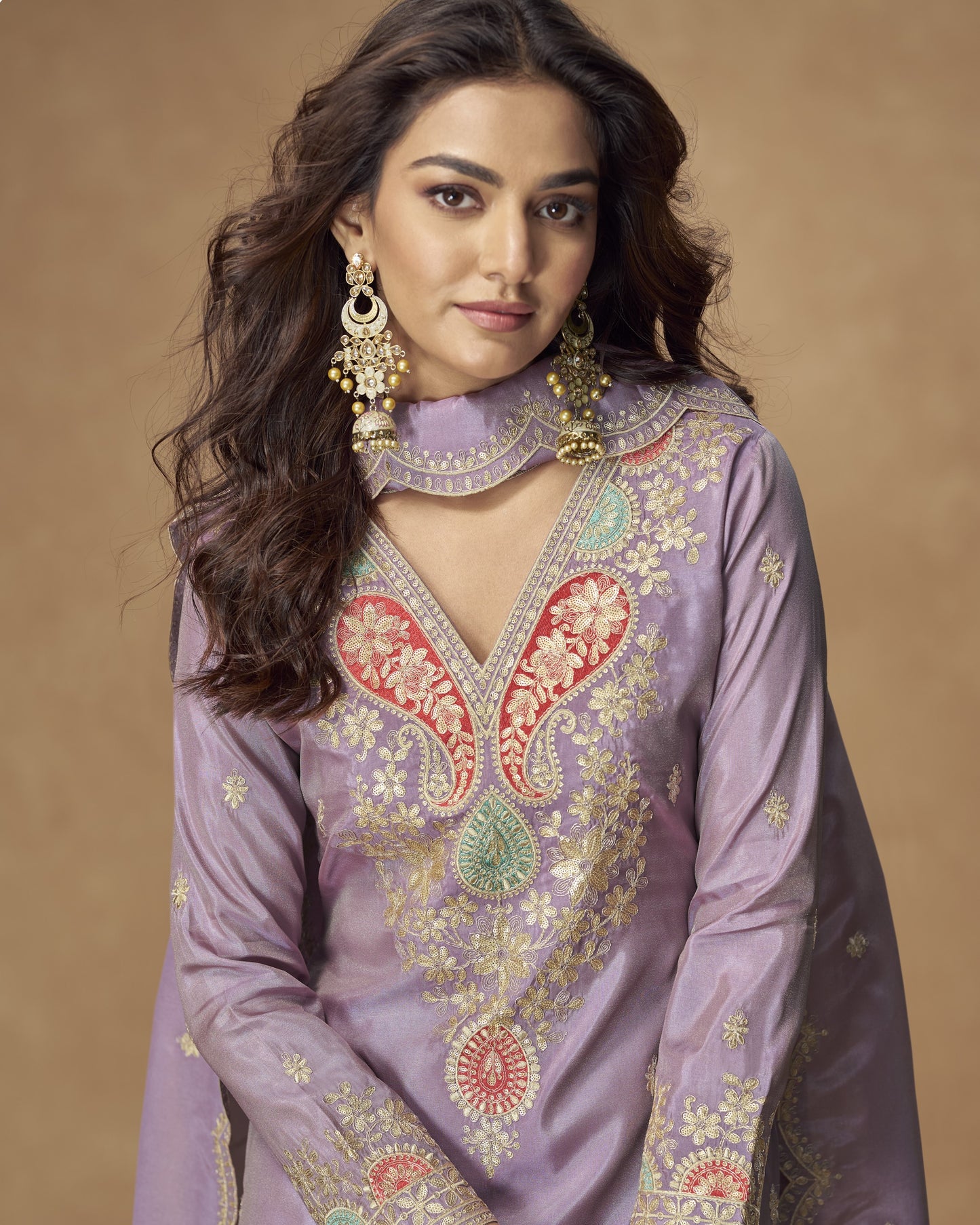 Woman wearing a purple embroidered traditional outfit with gold jewelry against a beige background