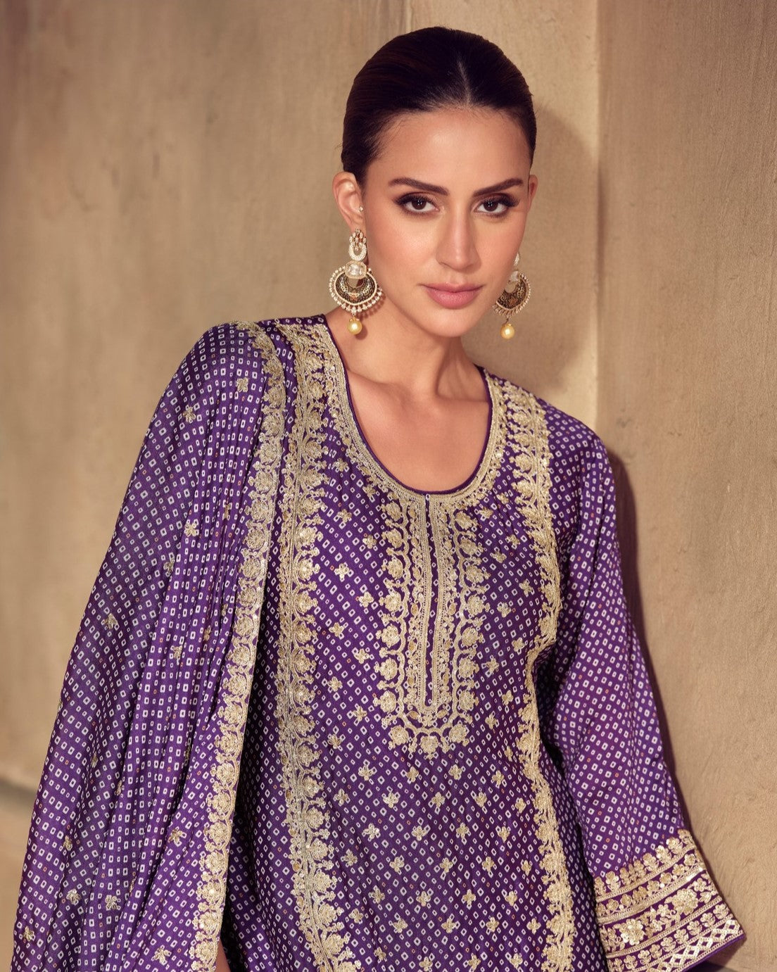 Woman wearing a purple embroidered outfit with gold details against a beige background