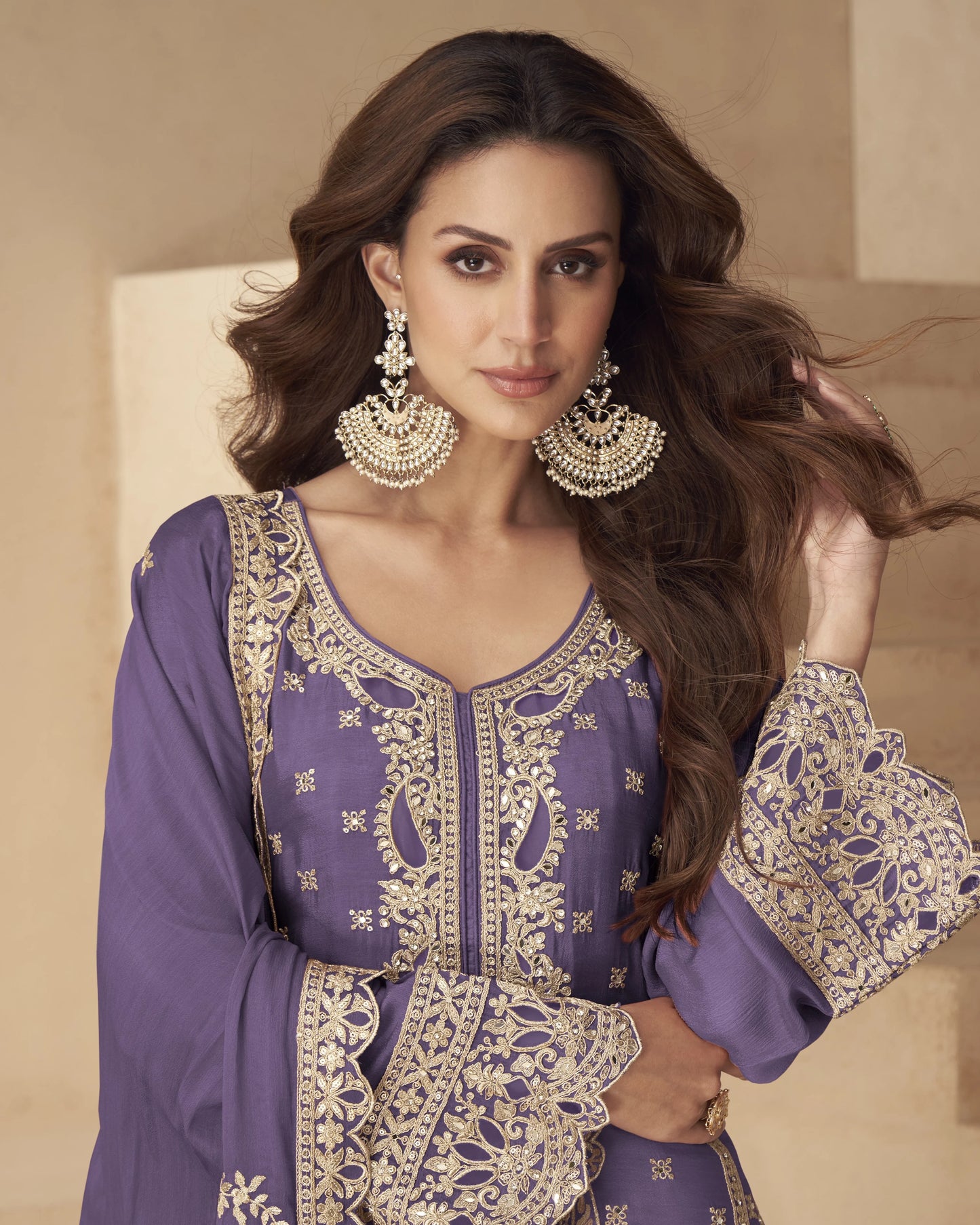 Woman wearing a purple and gold embroidered outfit with jewelry against a beige background