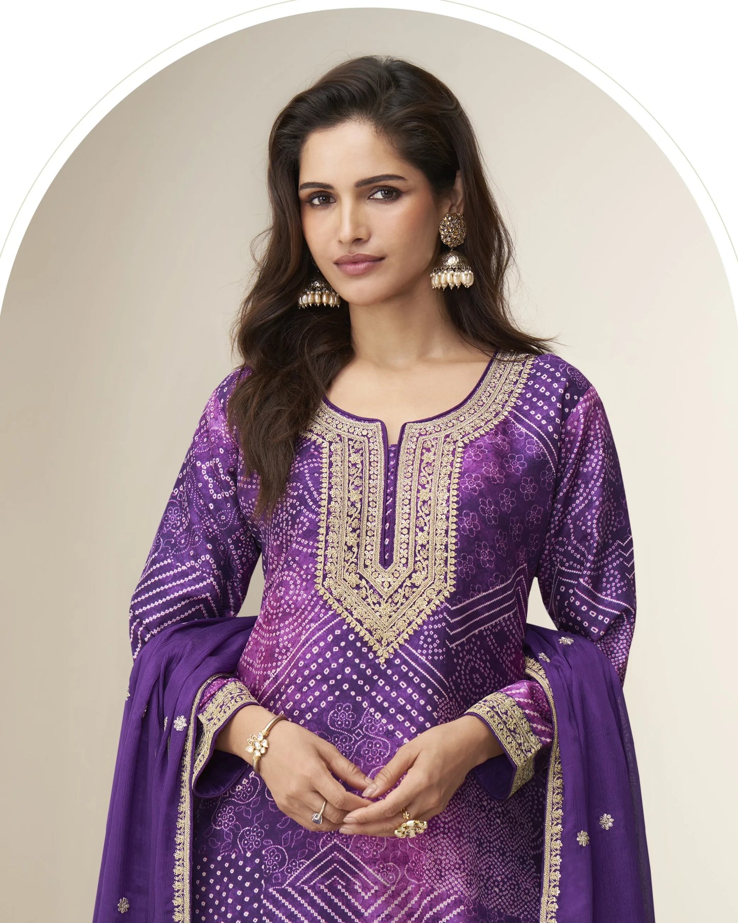 Woman wearing a purple embroidered traditional outfit with gold details on a beige background
