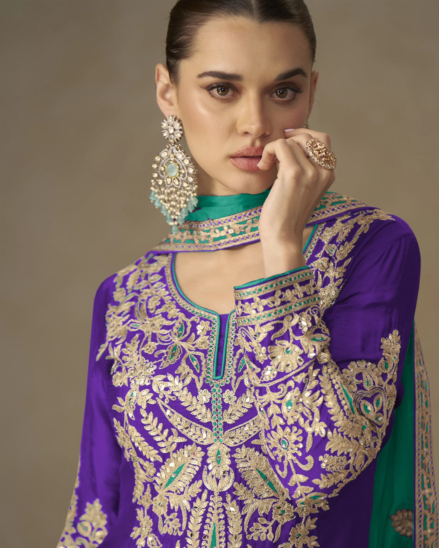 Woman wearing a purple and green embroidered traditional outfit with jewelry against a neutral background
