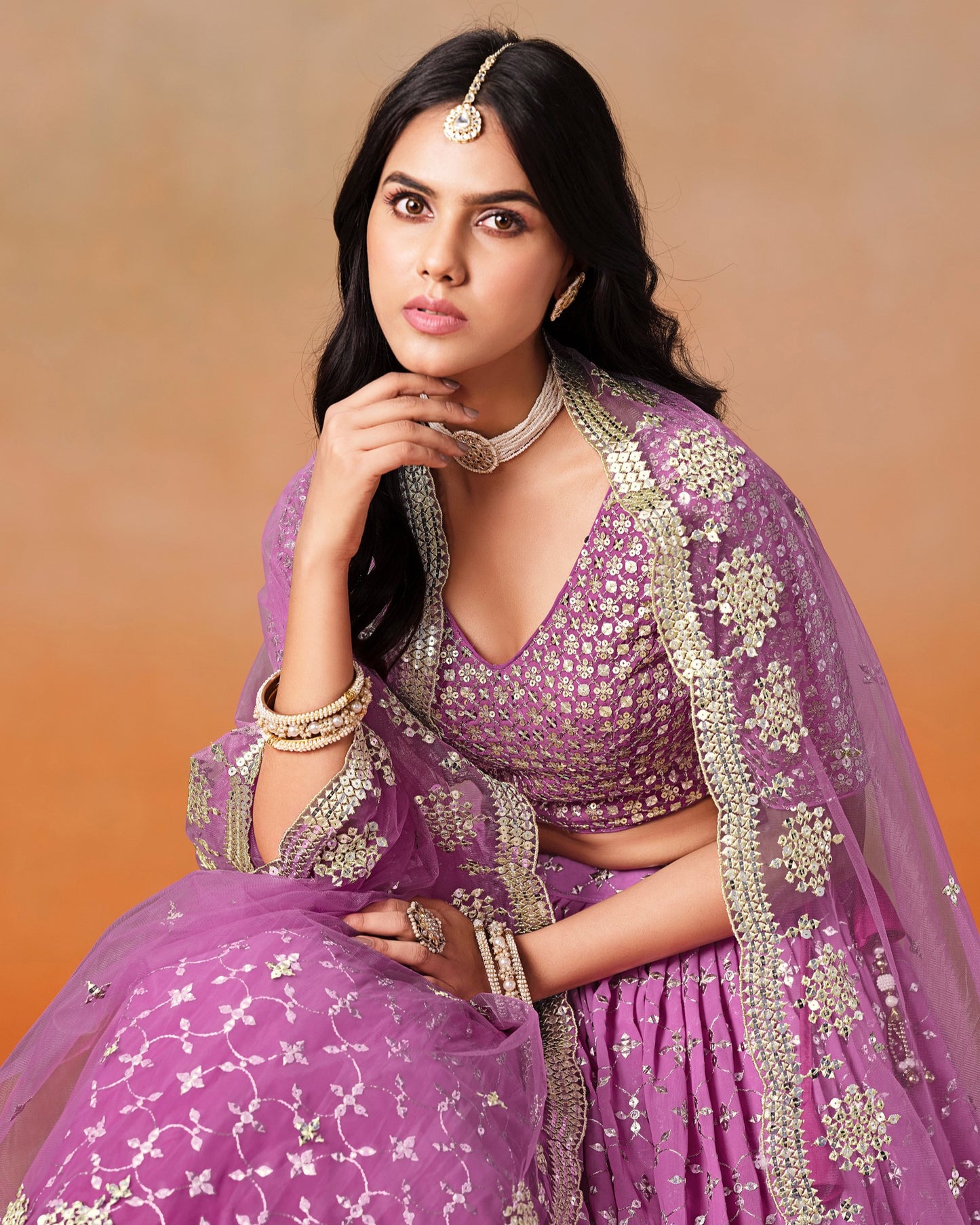 Woman in a purple traditional outfit with intricate designs against a warm gradient background