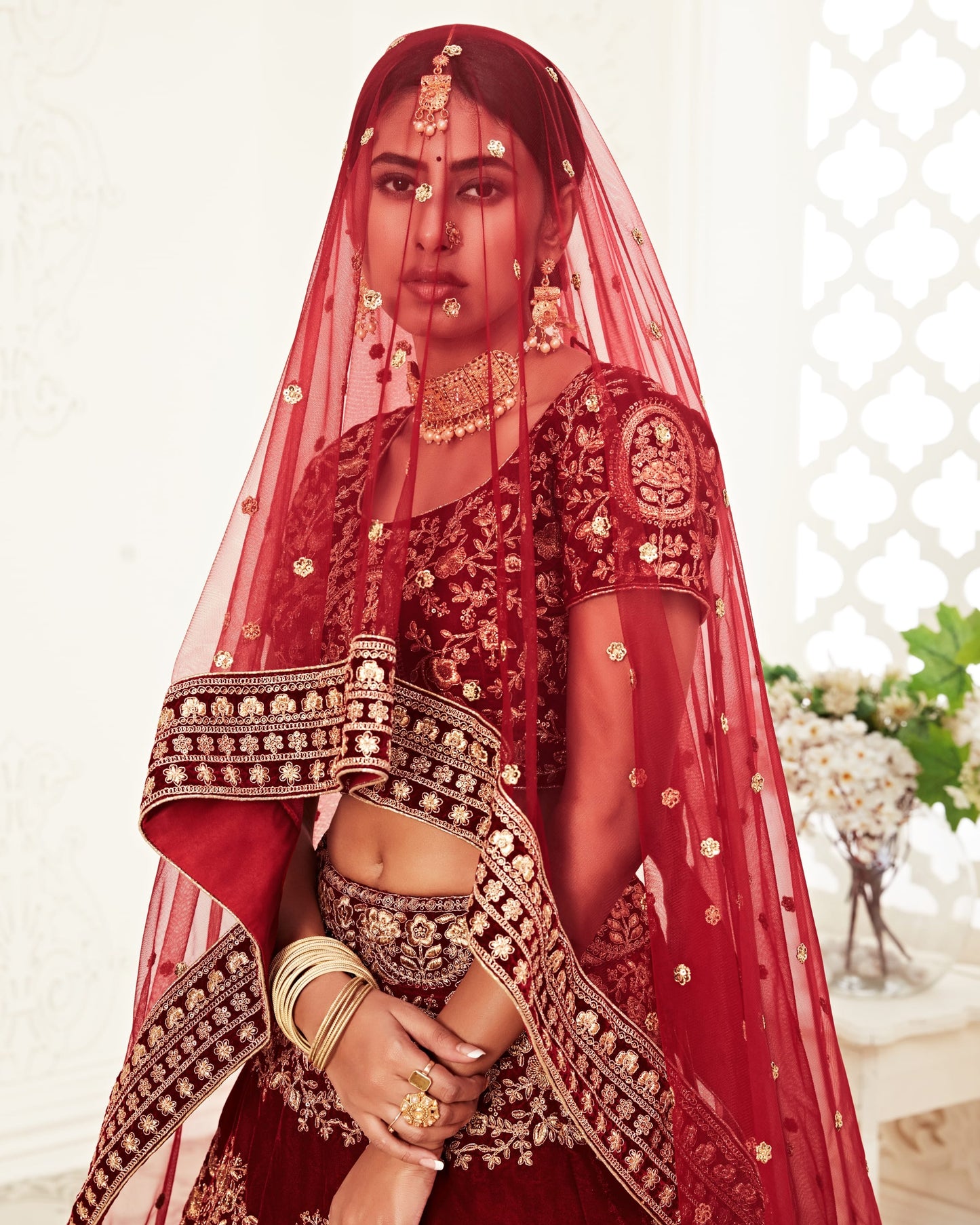 Woman in traditional red bridal outfit with intricate designs and jewelry.
