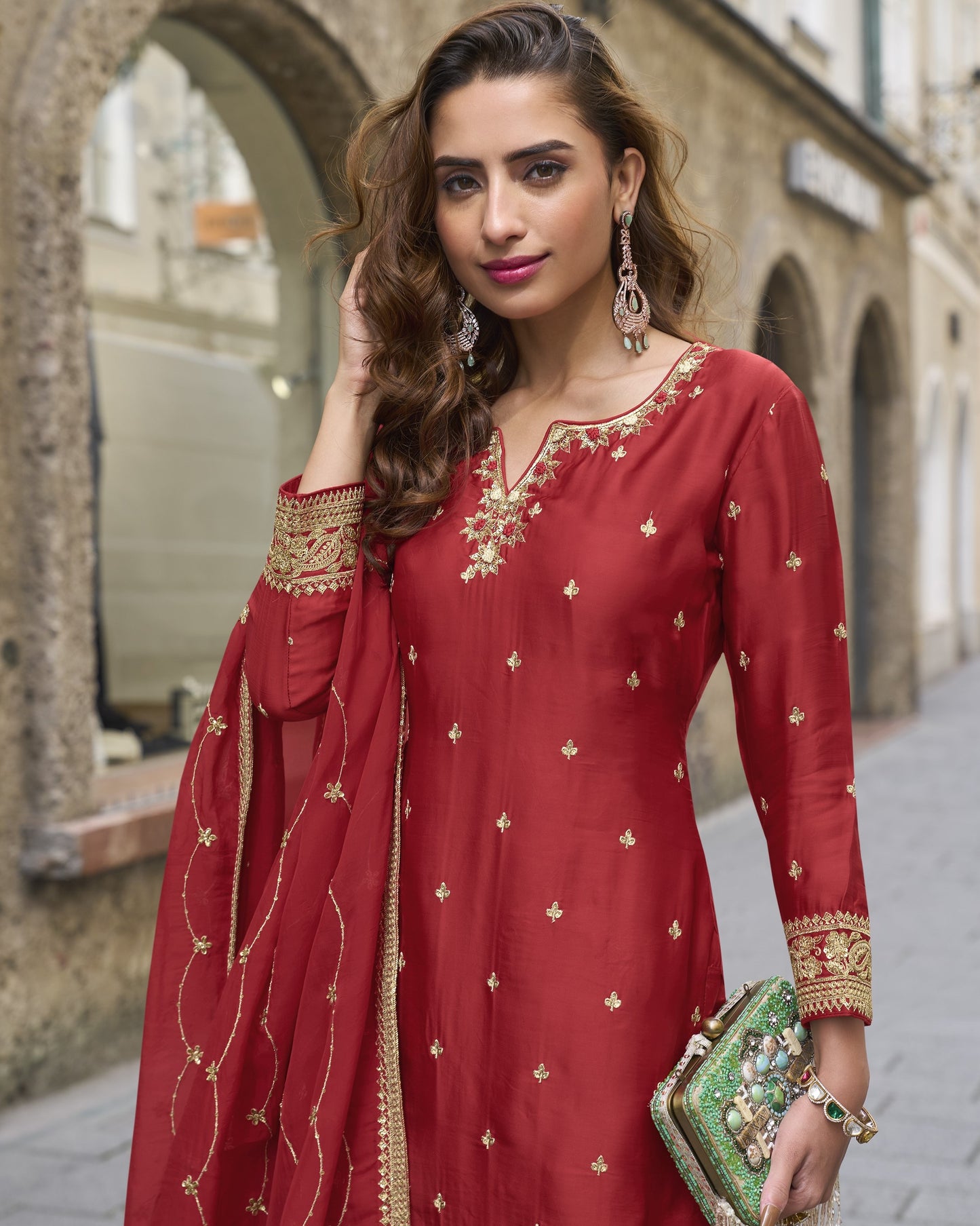 Woman in a red traditional outfit with gold embroidery standing outdoors.