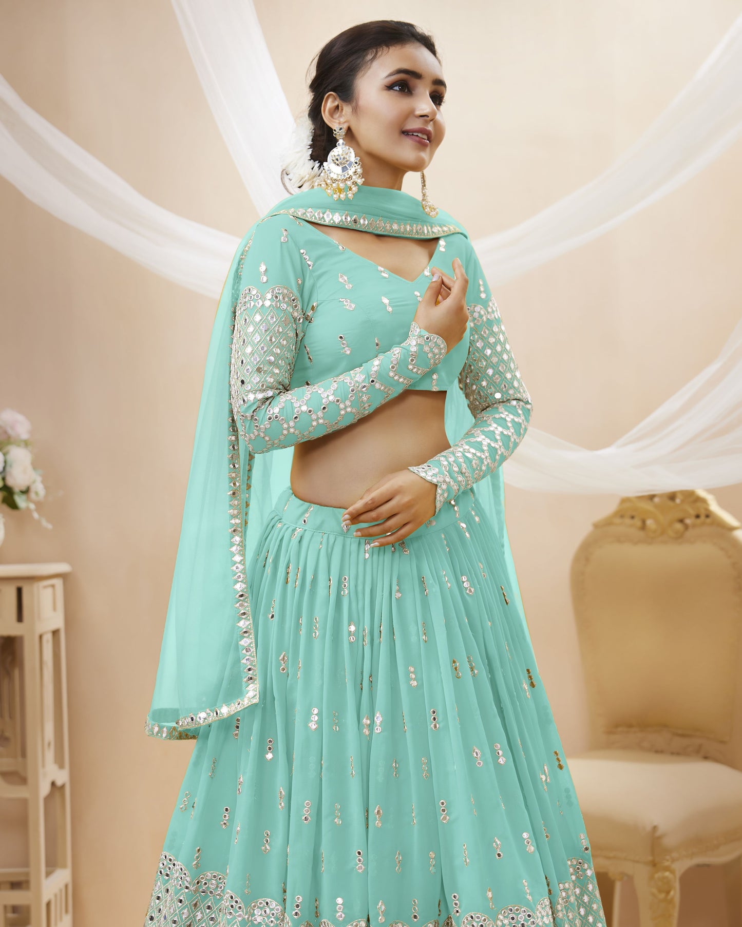 Woman wearing a light blue traditional outfit with silver embroidery in a decorated room.
