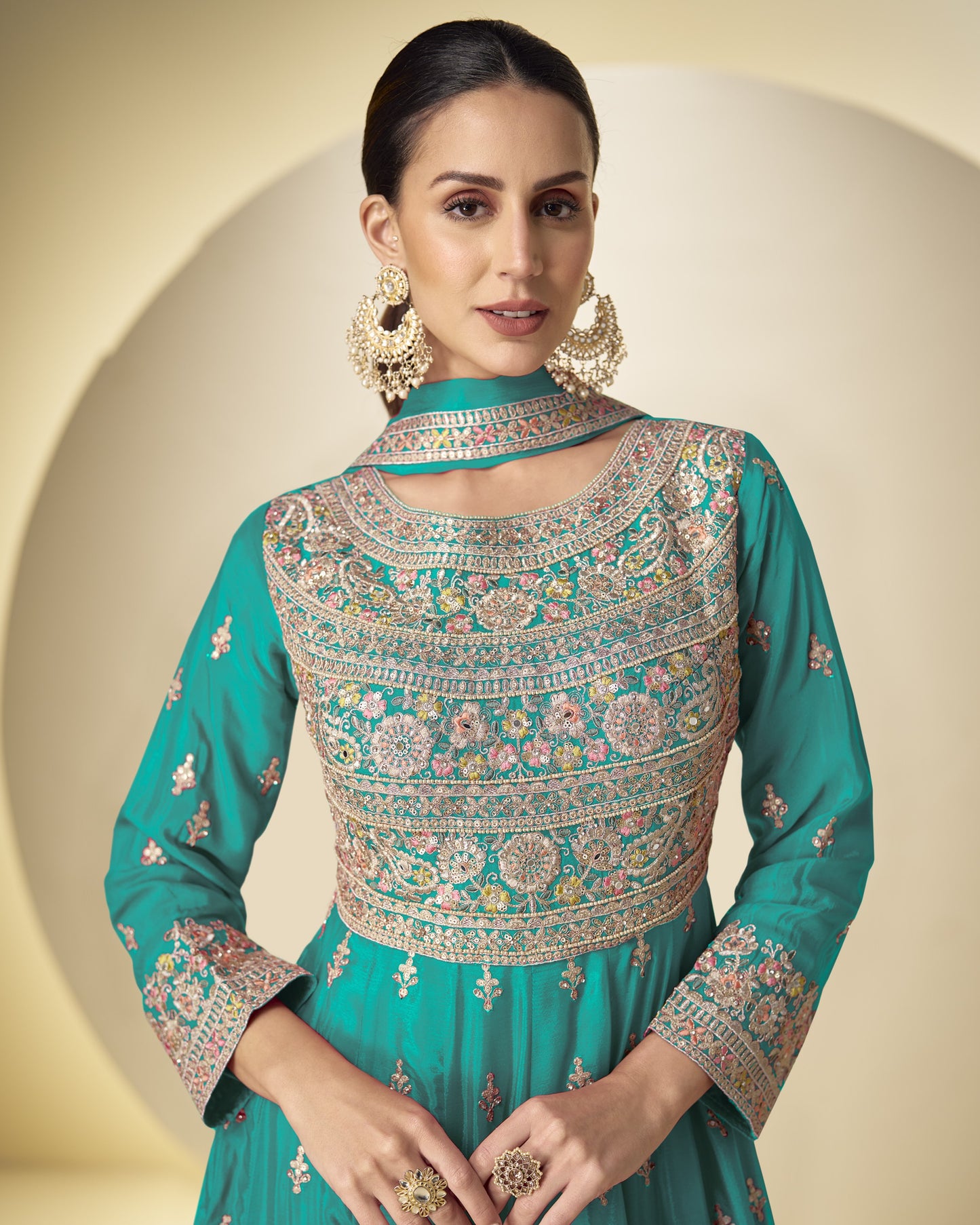Woman wearing a teal embroidered traditional outfit with a beige background