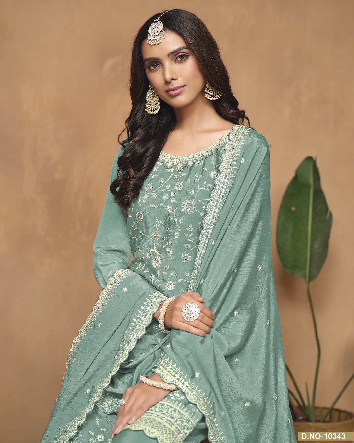 Woman wearing a green traditional outfit with intricate designs against a beige background