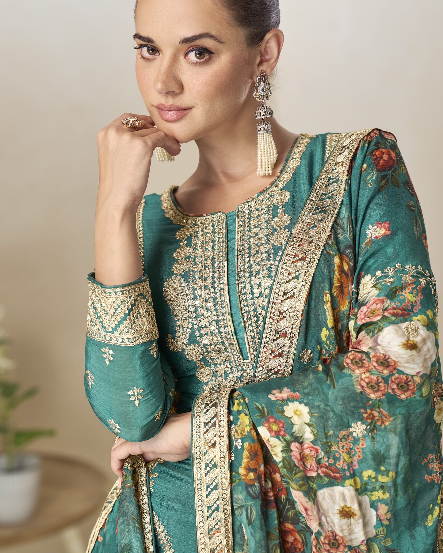 Woman wearing a teal embroidered traditional outfit with floral patterns indoors.
