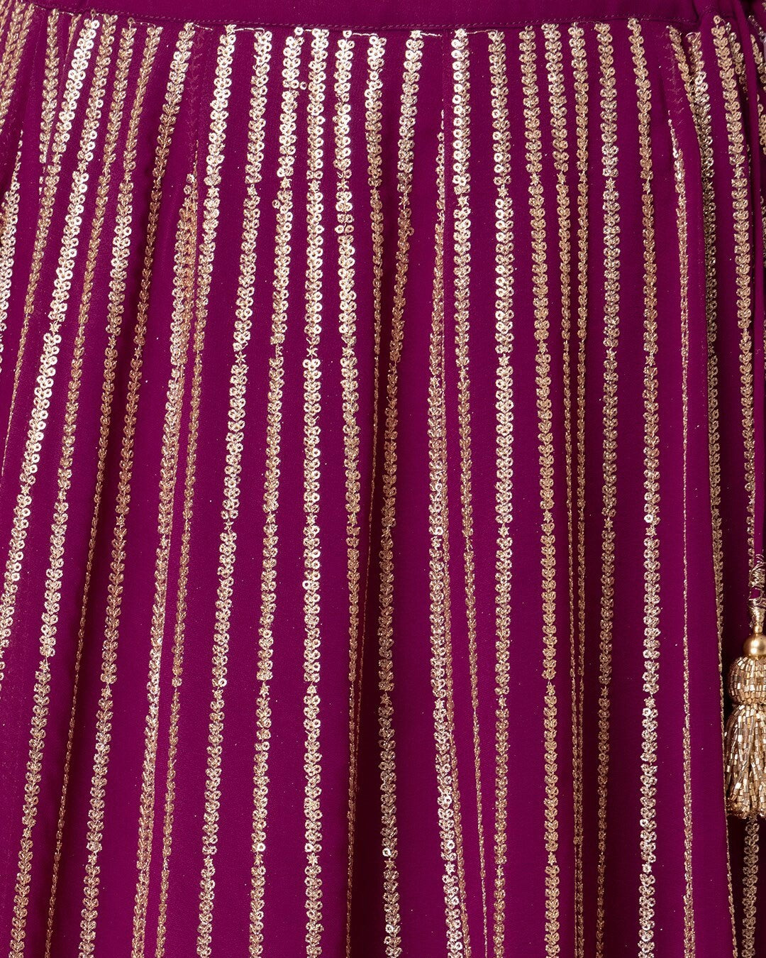 Close-up of a purple fabric with gold thread patterns and tassels.