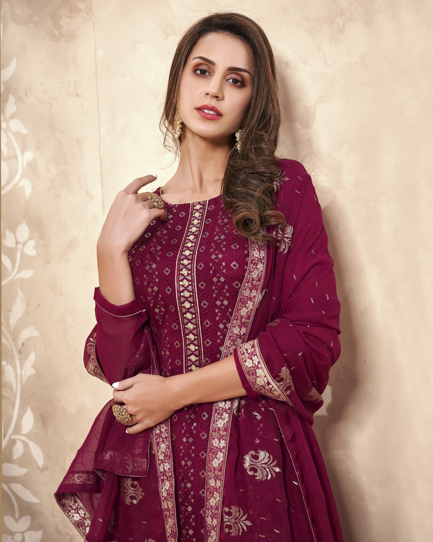 Woman wearing a maroon traditional outfit with intricate patterns against a beige background