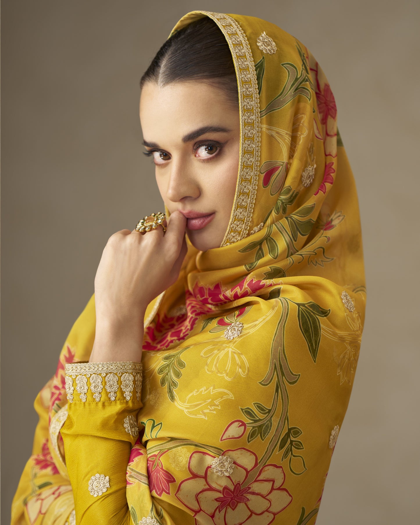 Woman wearing a yellow floral embroidered headscarf against a brown background